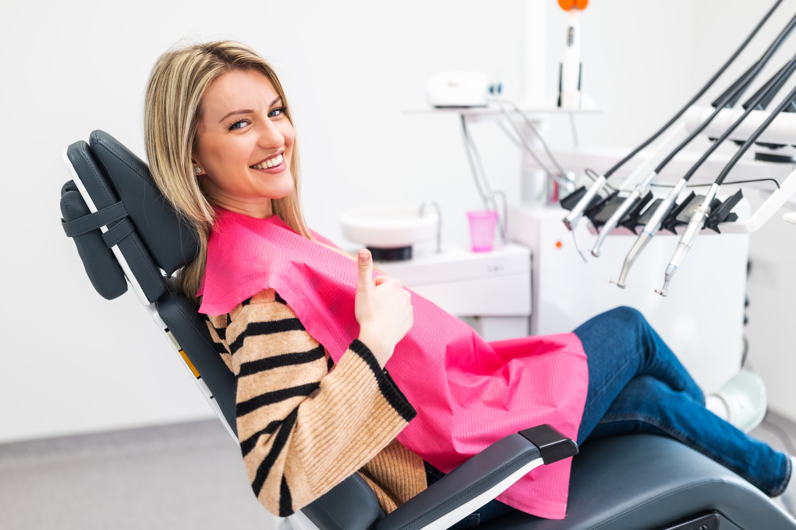 Happy young woman at dental clinic. Professional dental care and hygiene. She is showing thumbs up.