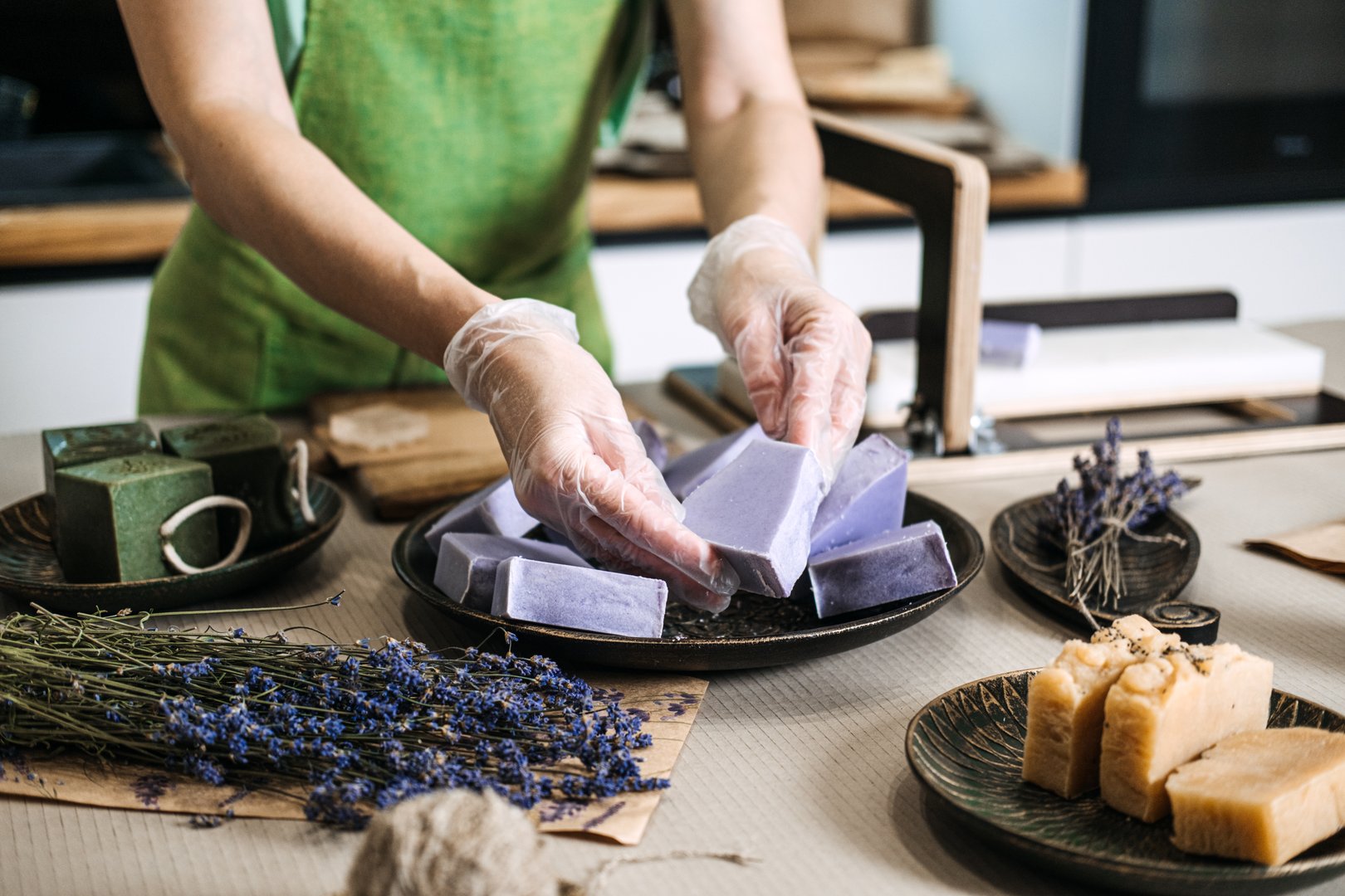 Close-up of hands placing lavender handmade soap bars on a tray with dried lavender. Focus on craft, organic skincare, and small business production.