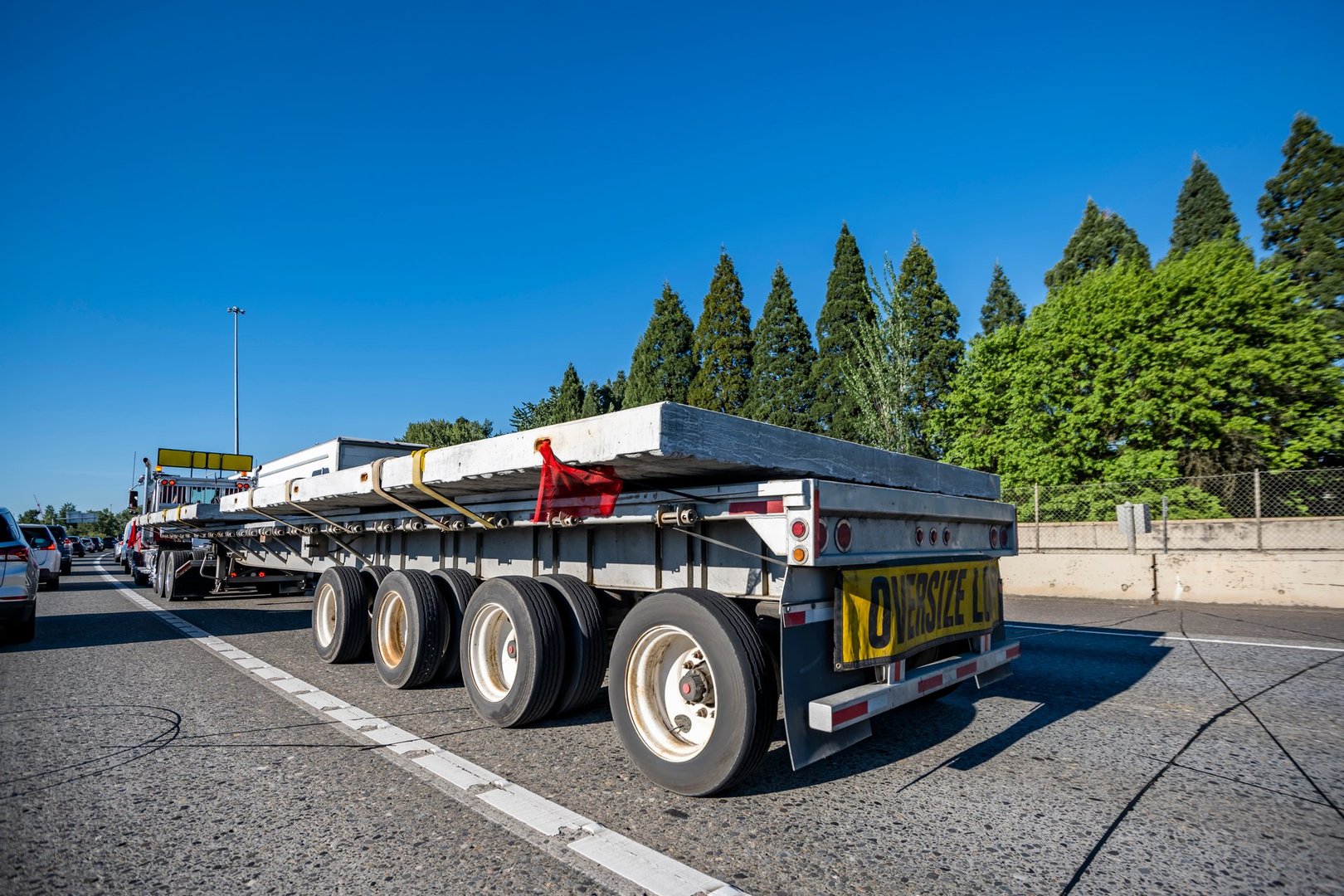 Industrial carrier red day cab big rig semi truck with oversize load sign transporting oversized cargo on flat bed semi trailer running on the wide highway road