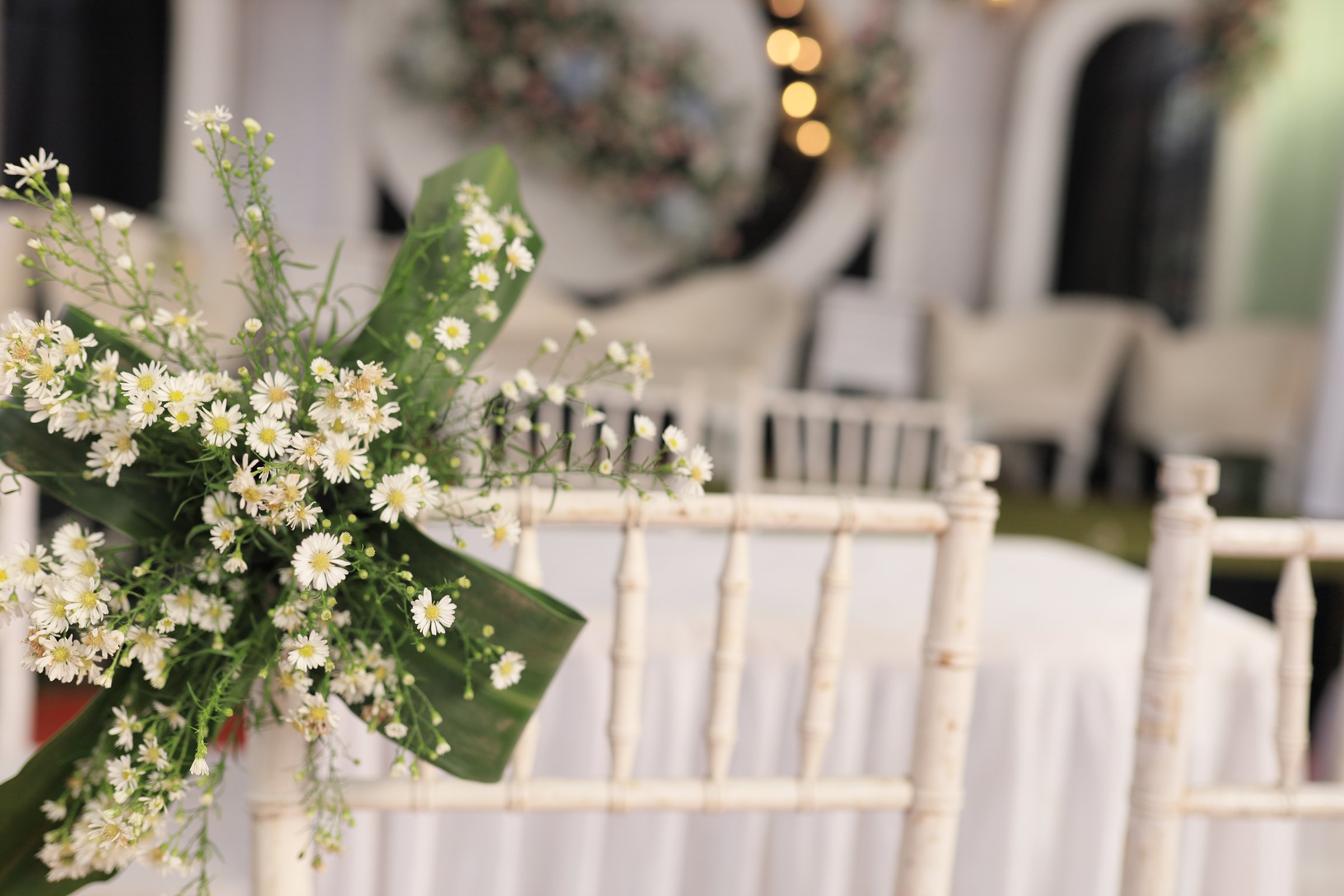 A delicate floral detail sets a romantic and serene atmosphere at an elegant wedding venue. With the main stage softly out of focus in the background, this image captures the quiet beauty and anticipation of a celebration of love, focusing on the small, elegant touches that make the day feel special. A perfect scene of romantic preparation.