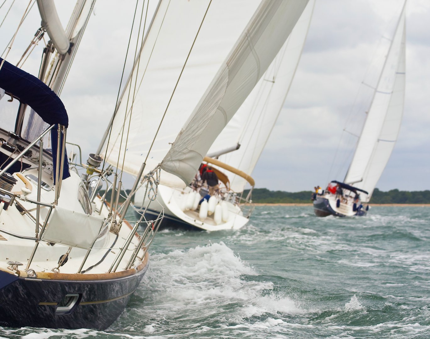 Three beautiful yachts sailboats with white sails racing close to each other on a bright sunny day