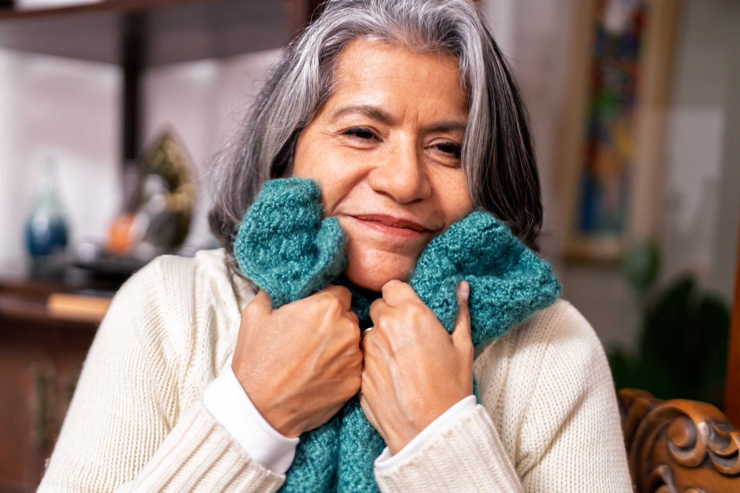Happy mature woman holding a hand-knitted shawl, embracing the warmth and comfort it brings while radiating joy and contentment