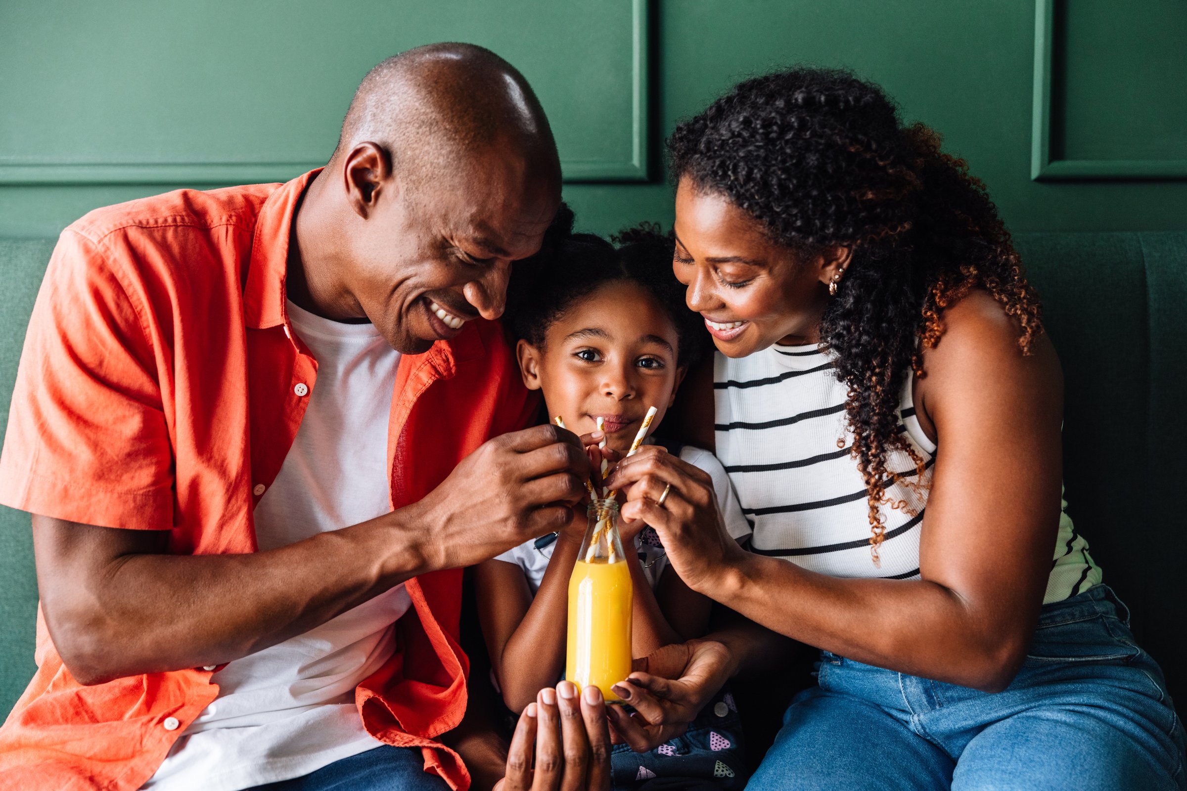 Happy black family laugh and smile together as they have fun drinking a juice together in a cozy home setting.