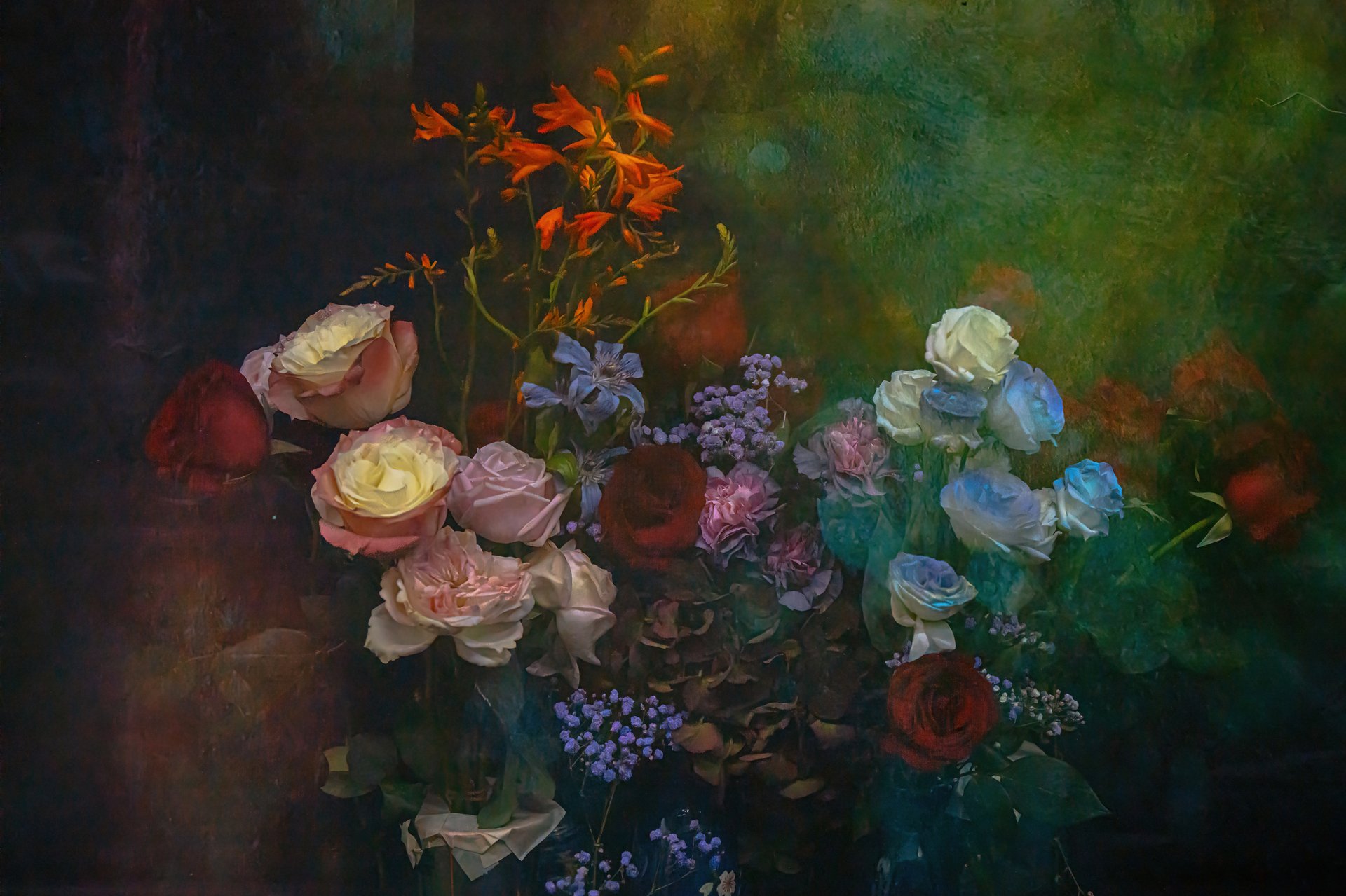 This photo showcases a lush and vibrant arrangement of various flowers, blending soft pastels with rich, bold tones. Roses in shades of white, pink, and red are complemented by delicate blue blossoms and fiery orange stems, creating a striking contrast. Set against a deep, textured background, the flowers appear to glow with an inner light, evoking the beauty of a flourishing garden in full bloom. The composition radiates elegance, inviting the viewer to appreciate the harmony and diversity of nature’s palette.