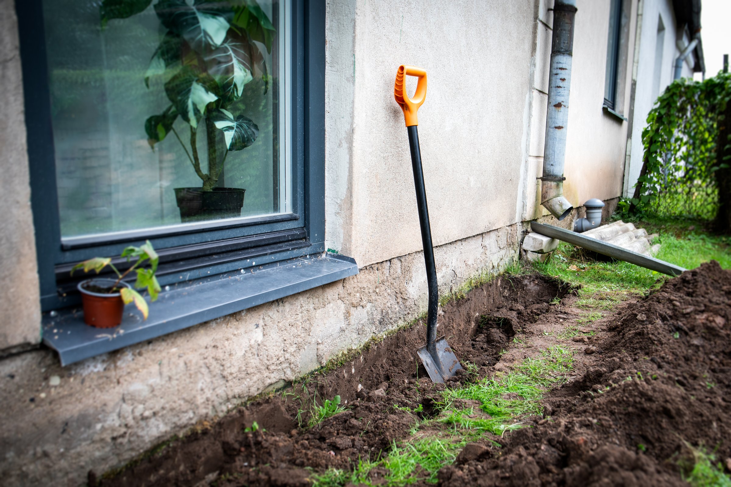 A trench at the foundation of the house and a shovel. Preparing for insulation and renovation of foundation.