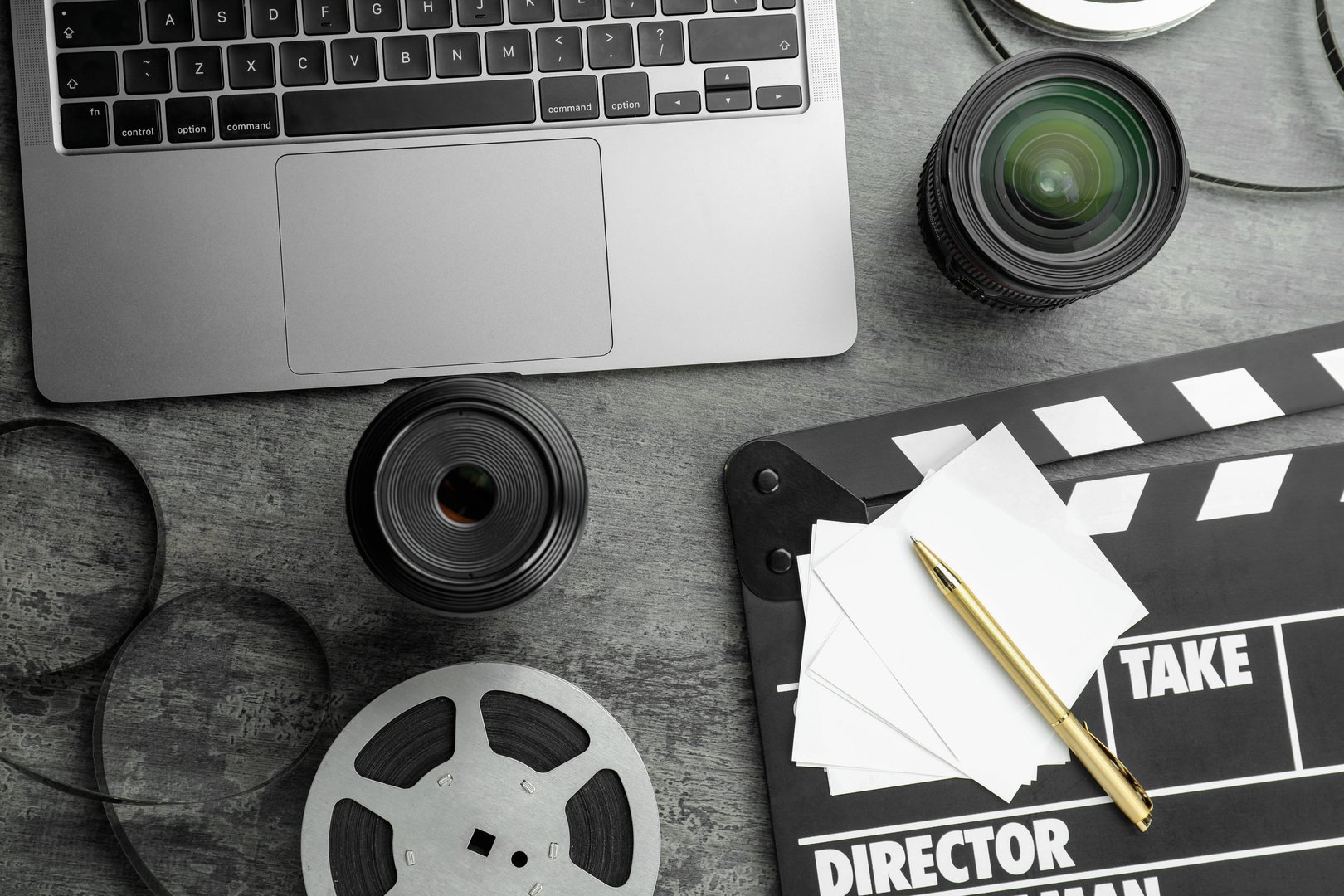 Flat lay composition with movie clapper, film reel and camera lens on grey textured table