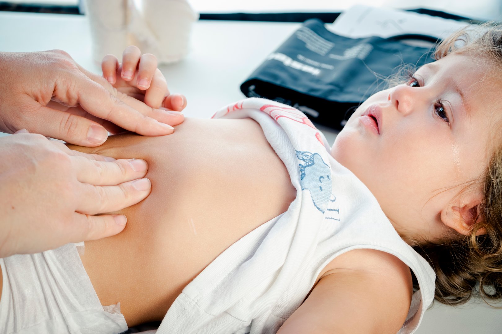 Female pediatrician doctor examining a baby's tummy with her hands, exploring the baby's health