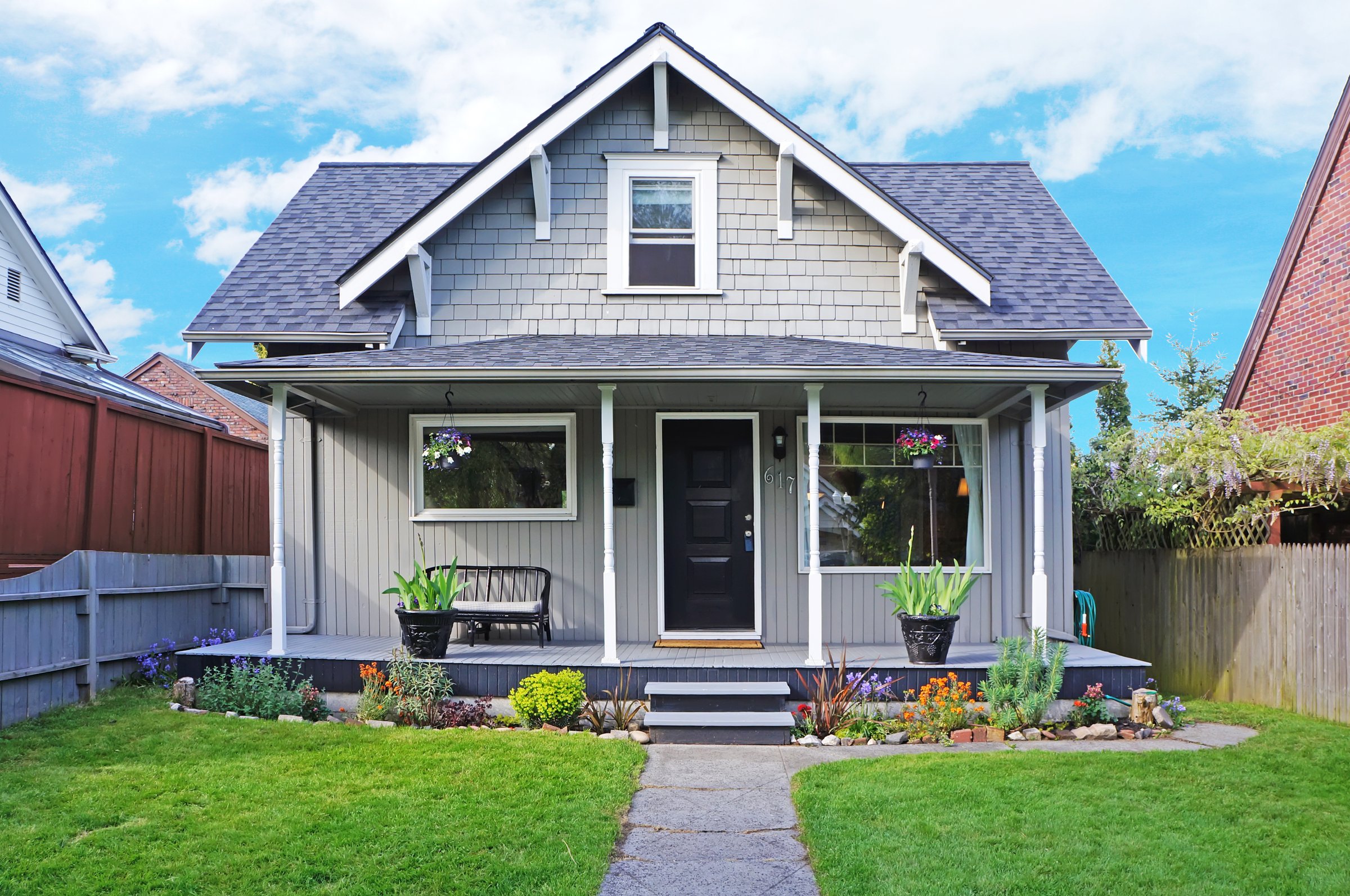 Small old house with entrance porch decorated with antique bench. Front yard has lawn and flower beds