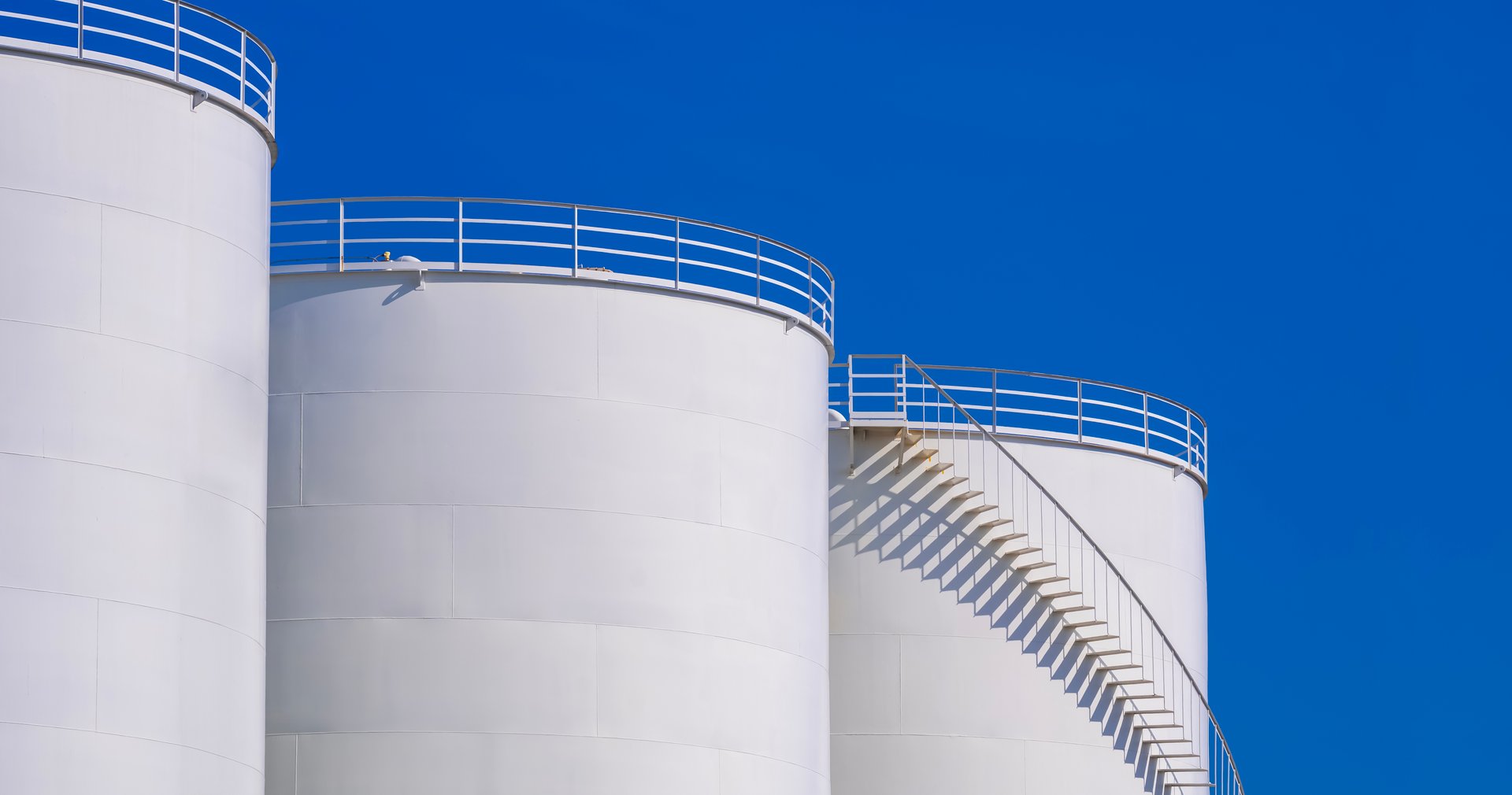 High section of 3 white storage fuel tanks in petroleum industry area against blue clear sky background