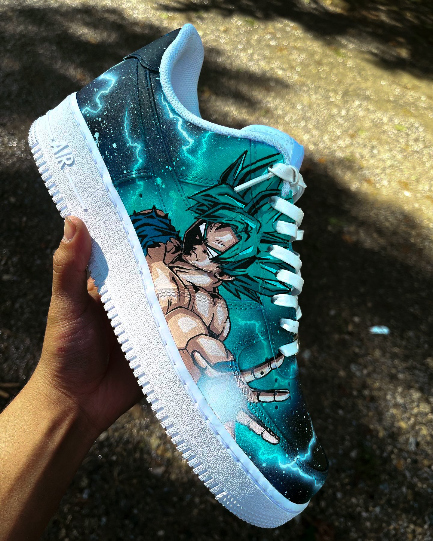 A custom sneaker with an anime character design, featuring electric blue and white colors, held by a persons hand.