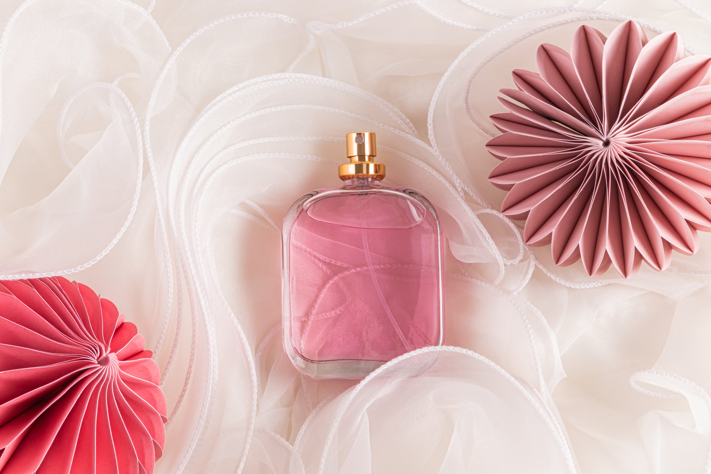 Empty non branded bottle of women's perfume on delicate beige wavy silk with eco Christmas toys. Product presentation. Perfume and beauty concept.