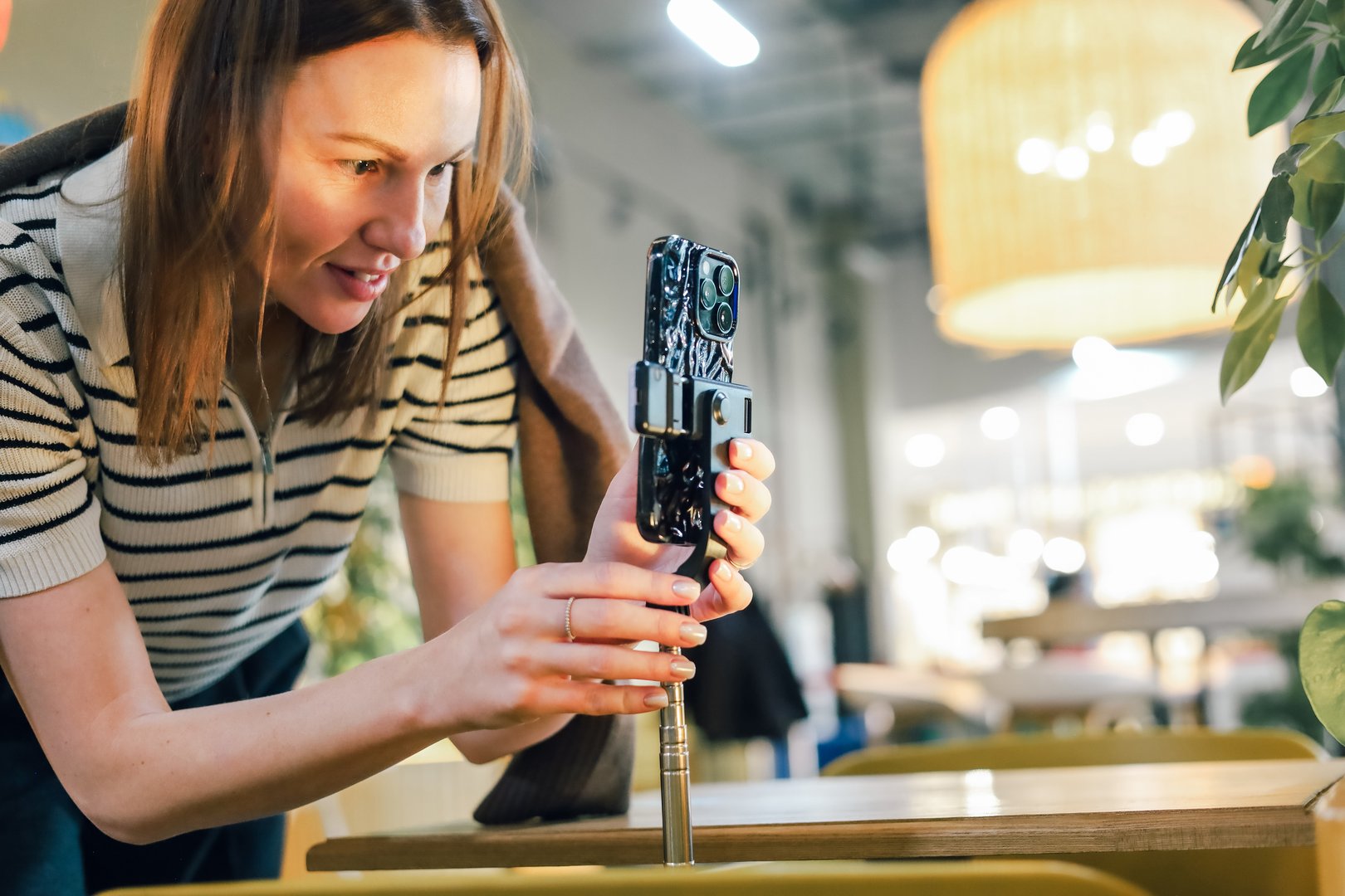 Focused woman adjusting a smartphone on a tripod, preparing to record or photograph content in a bright modern space, highlighting creativity, technology use and digital workflow.