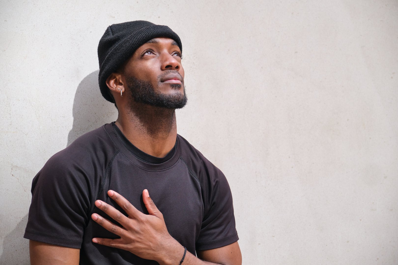 Young black man standing with hand over heart while looking up with hope