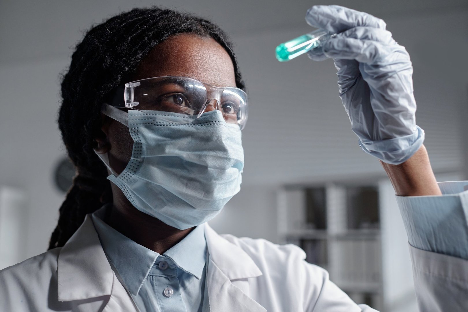 Female scientist engrossed in experiment while holding test tube in laboratory environment. Wearing safety goggles and protective mask for safety measures