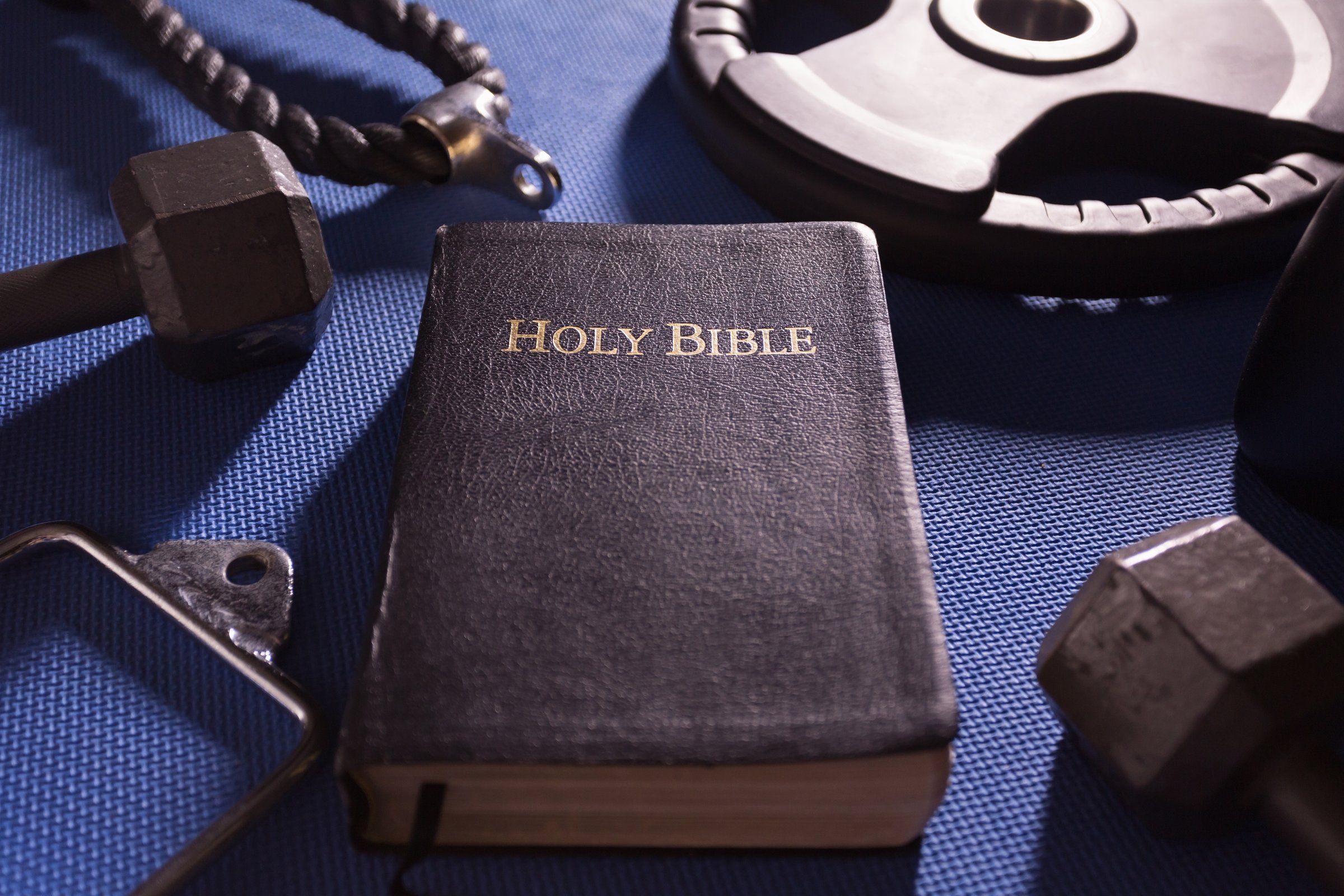 Holy Bible surrounded by dumbbells weights and other exercise equipment