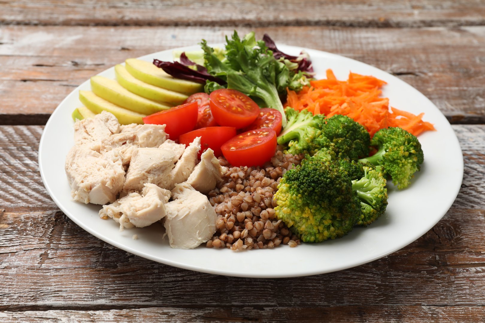 Balanced diet and healthy foods. Plate with different delicious products on wooden table, closeup