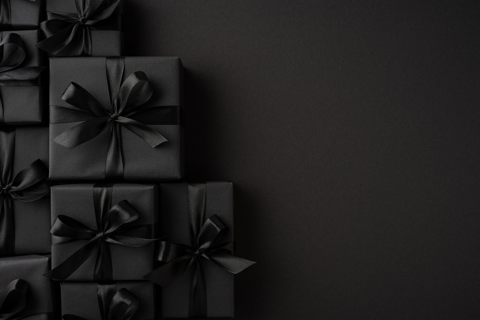 Luxurious black gift boxes with tied ribbons displayed on a solid dark backdrop enhancing the sophisticated look