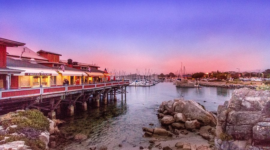 Scenic view of a waterfront with a pier, boats in the harbor, and a colorful sunset sky.