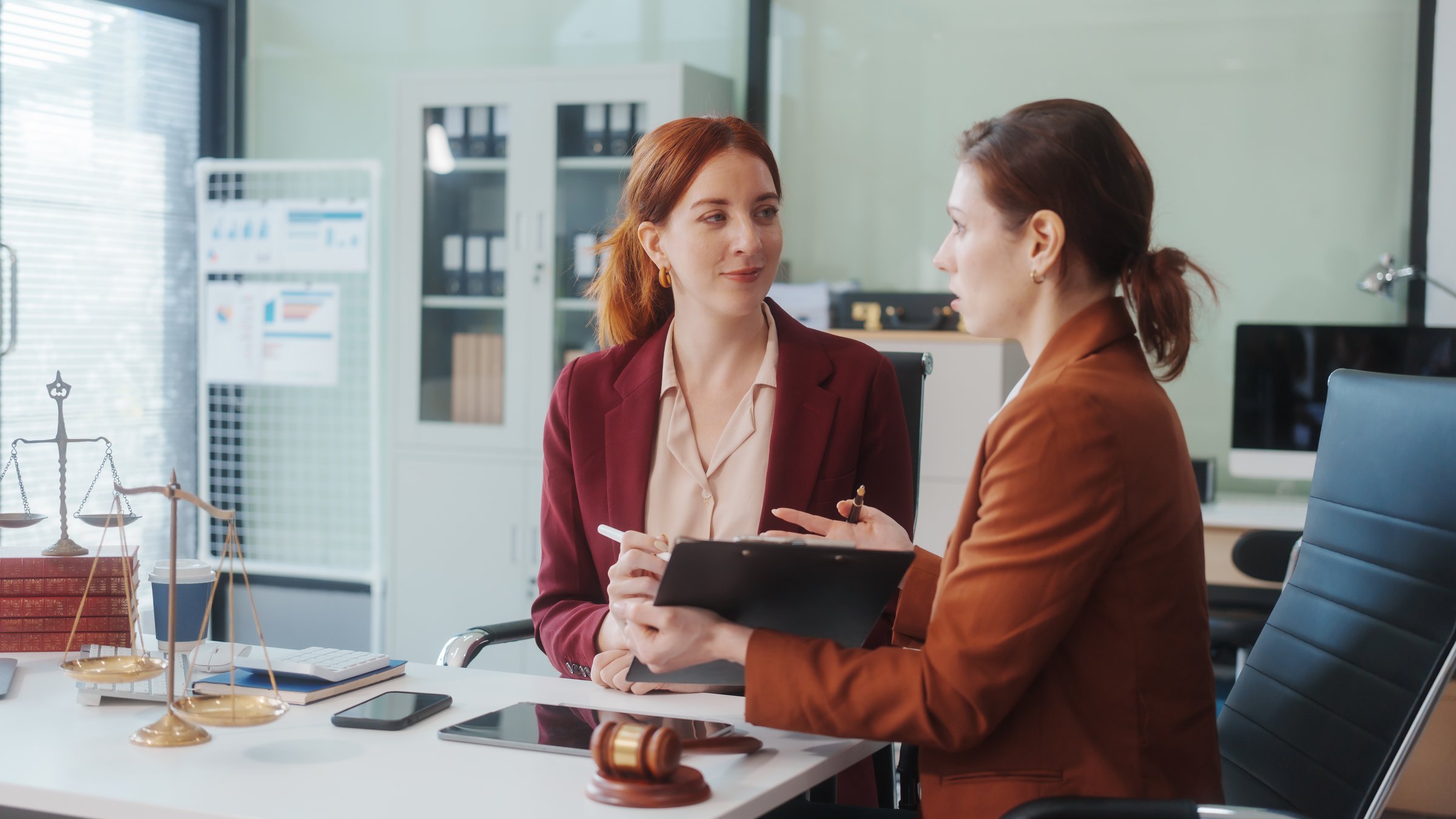 Two Caucasian women meet at a table, discussing legal matters. As lawyers, they advise clients on rights, responsibilities,business issues, representing them in criminal, civil, and regulatory cases