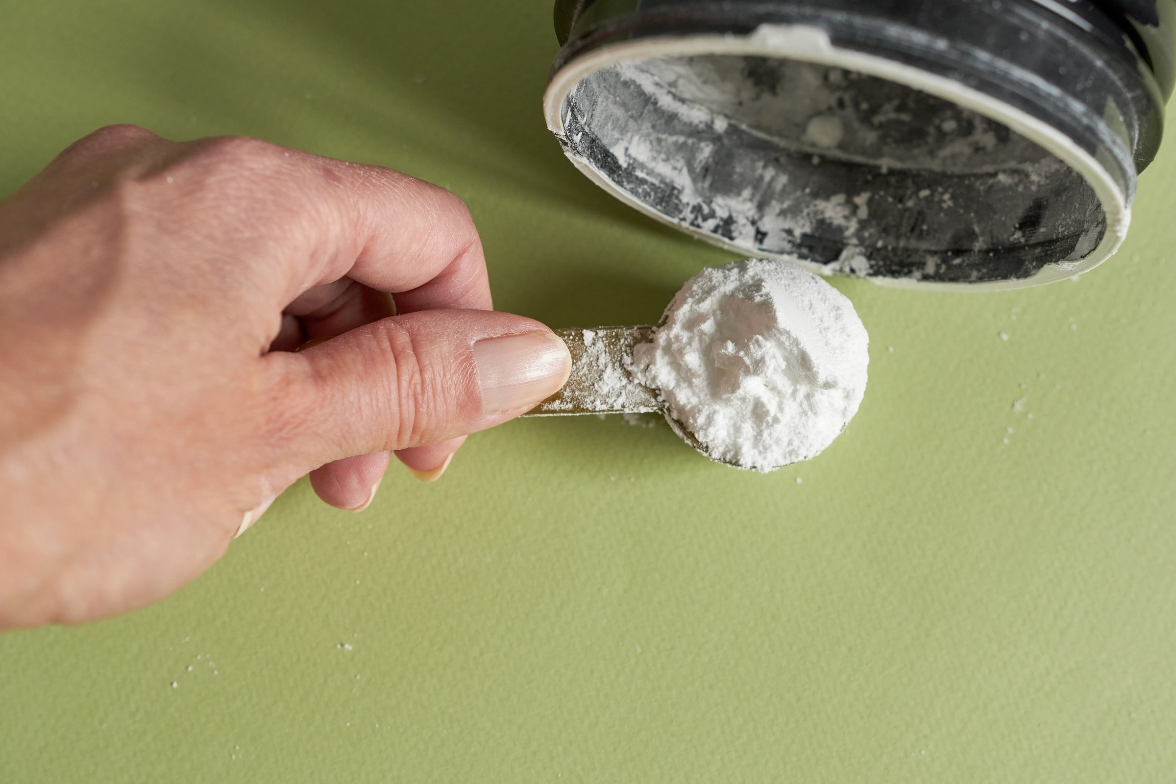 Close-up of a woman's hand, holding a measuring spoon of creatine. Creatine is a sports supplement.