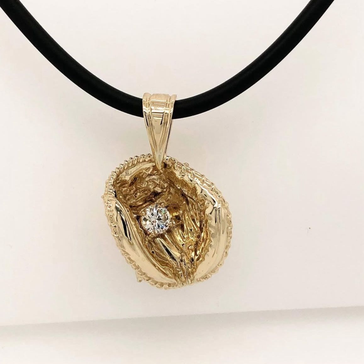 Gold walnut pendant with a diamond center on a black necklace cord, against a white background.
