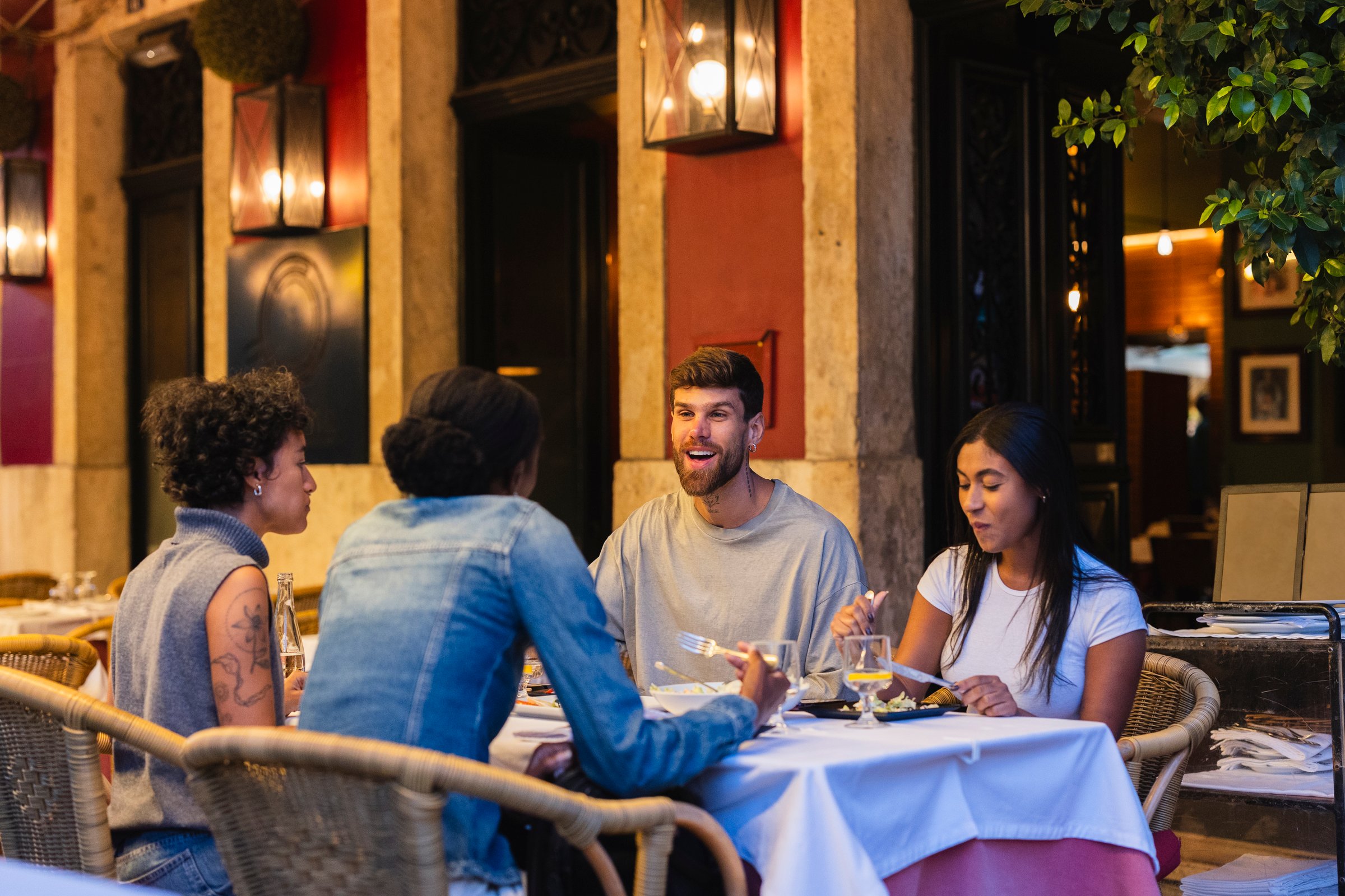 Four friends sitting around a table outside a restaurant in lisbon, portugal, enjoying a delightful meal and engaging in lively conversation under the warm evening sky
