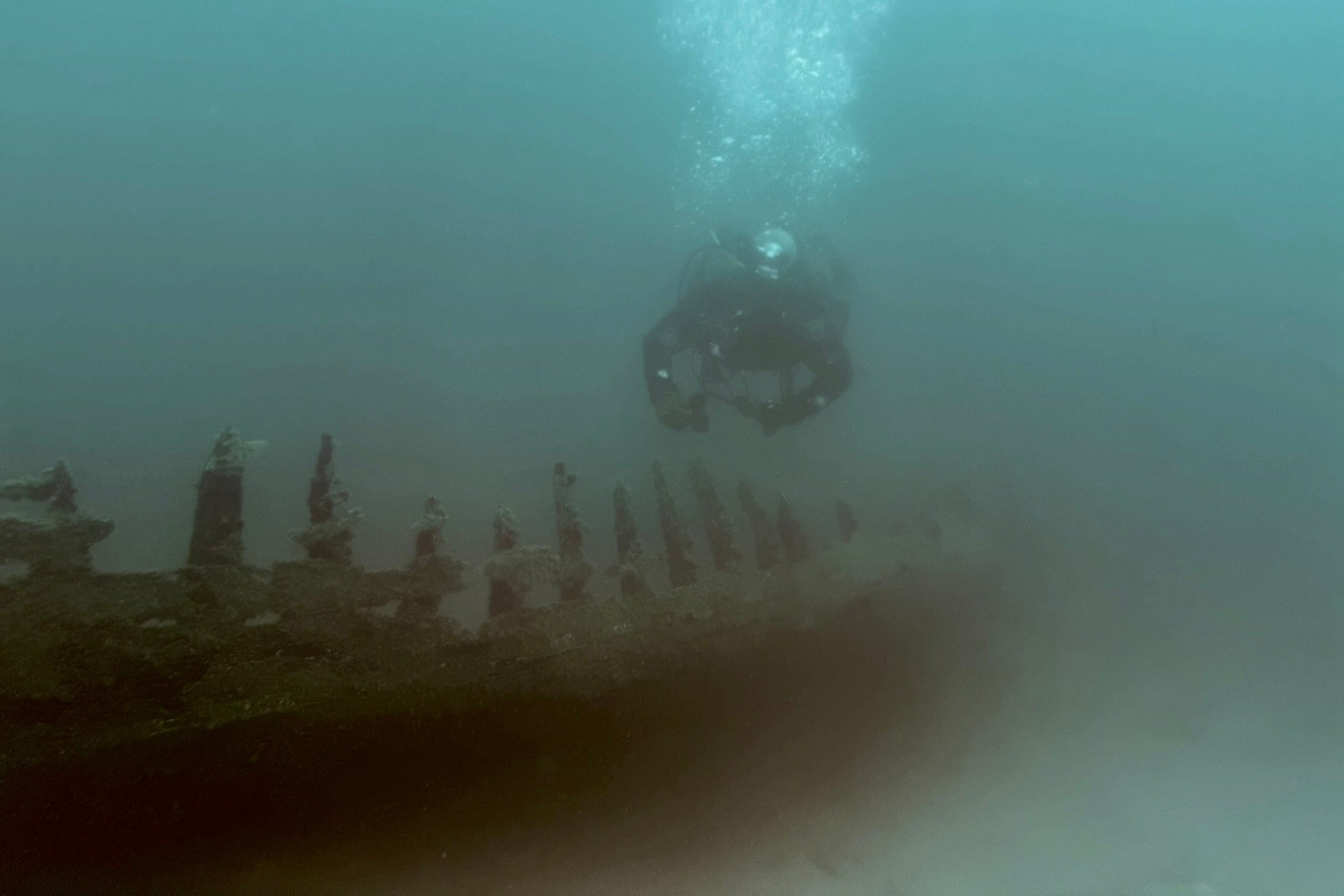 A scuba diver investigates the remains of a shipwreck under water, highlighting maritime exploration and underwater adventure.
