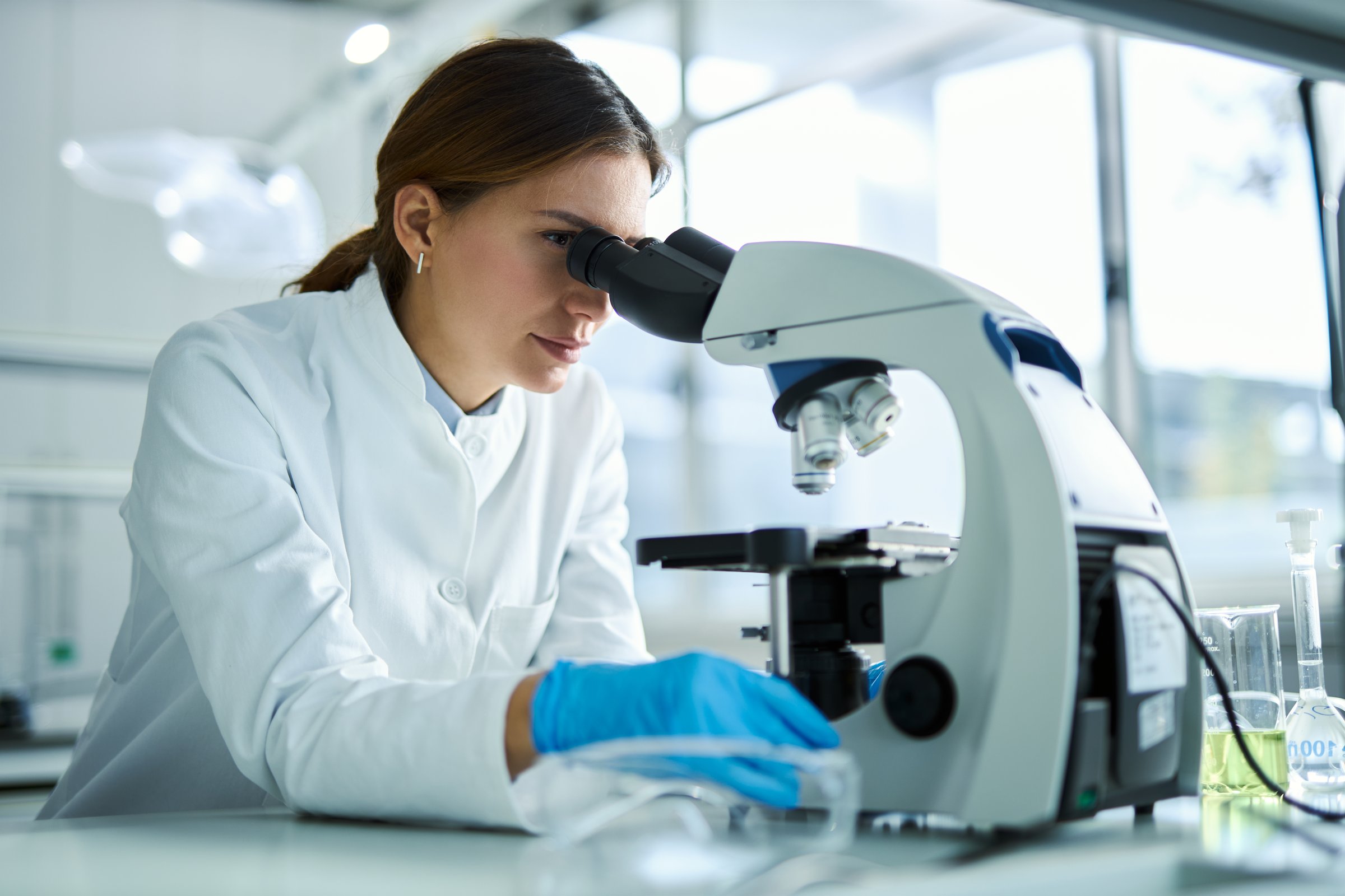 Young female scientist working on a research through a microscope in laboratory.