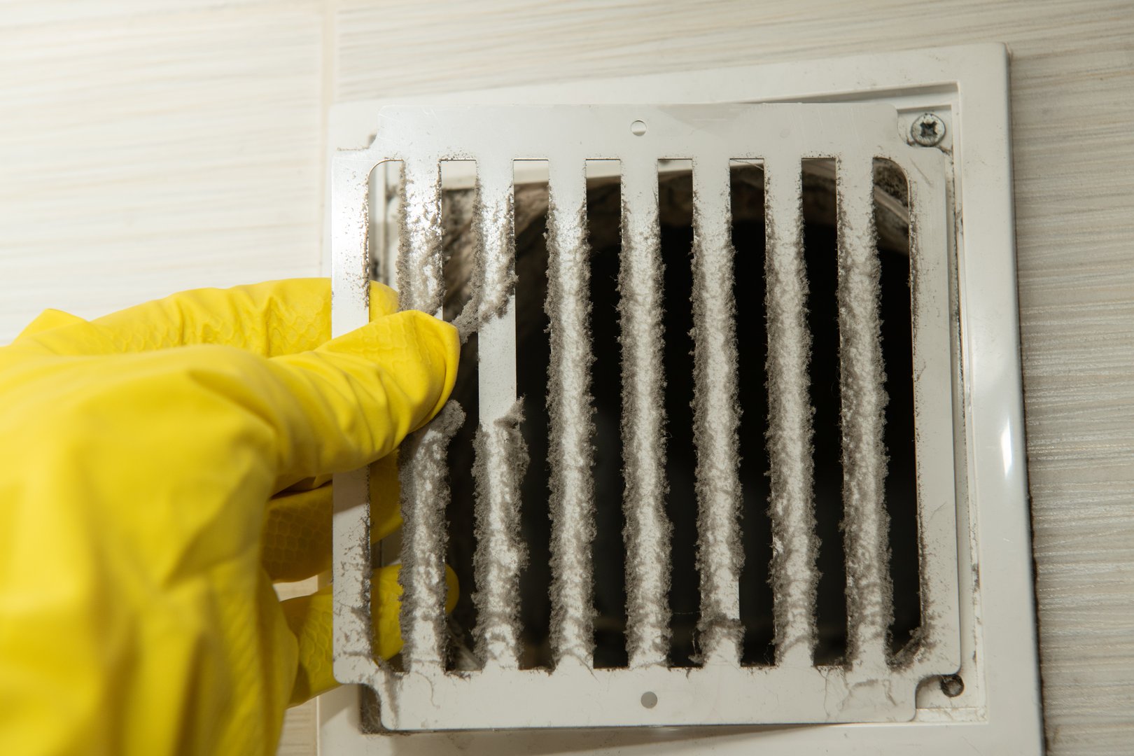 Hand wearing a yellow glove removes a significant amount of dust from a ventilation grill, promoting better indoor air quality and hygiene