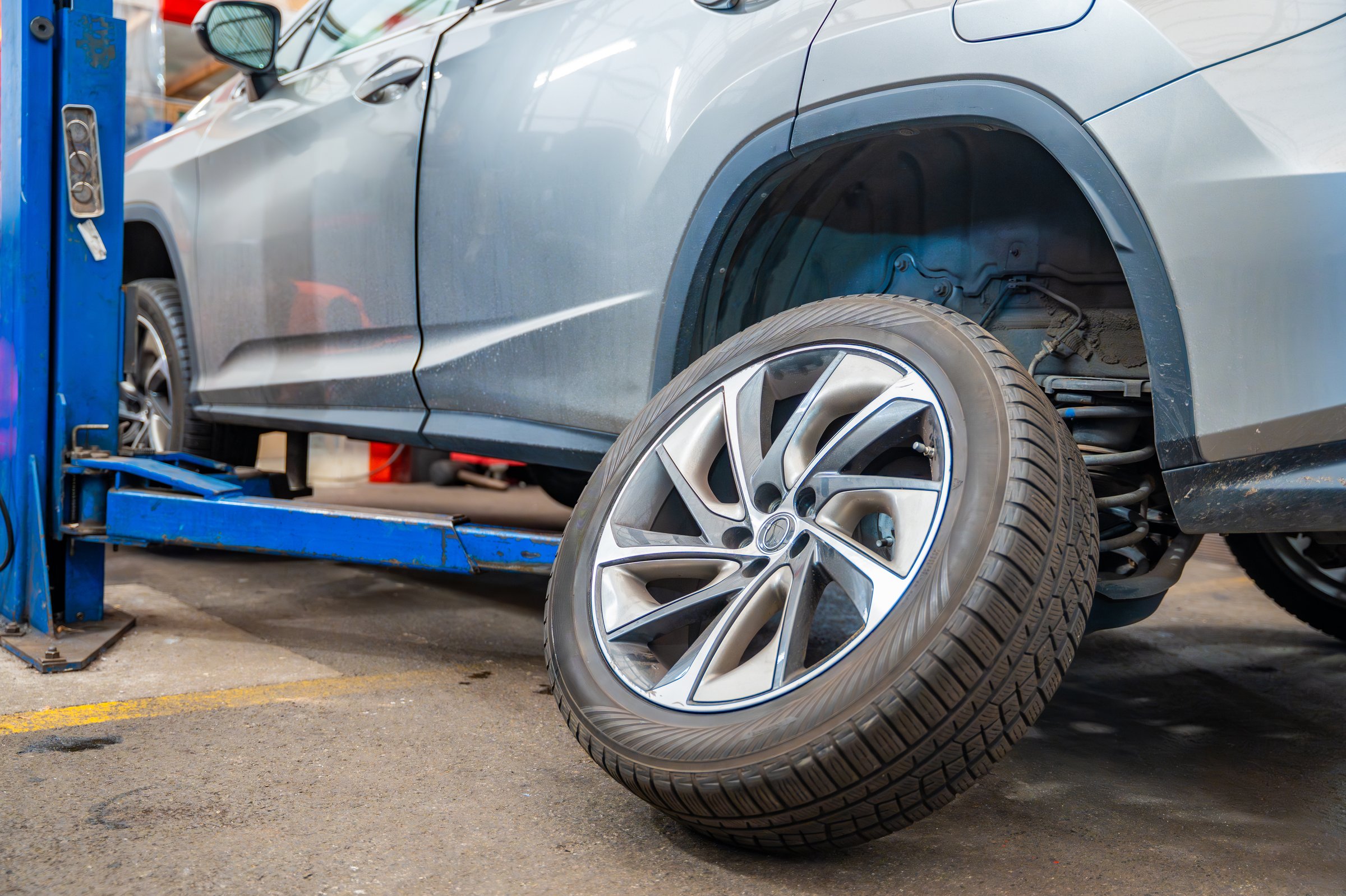 Prepared car wheel lying next to the vehicle before final installation. Seasonal tire change process during winter preparation at auto service workshop. High quality photo