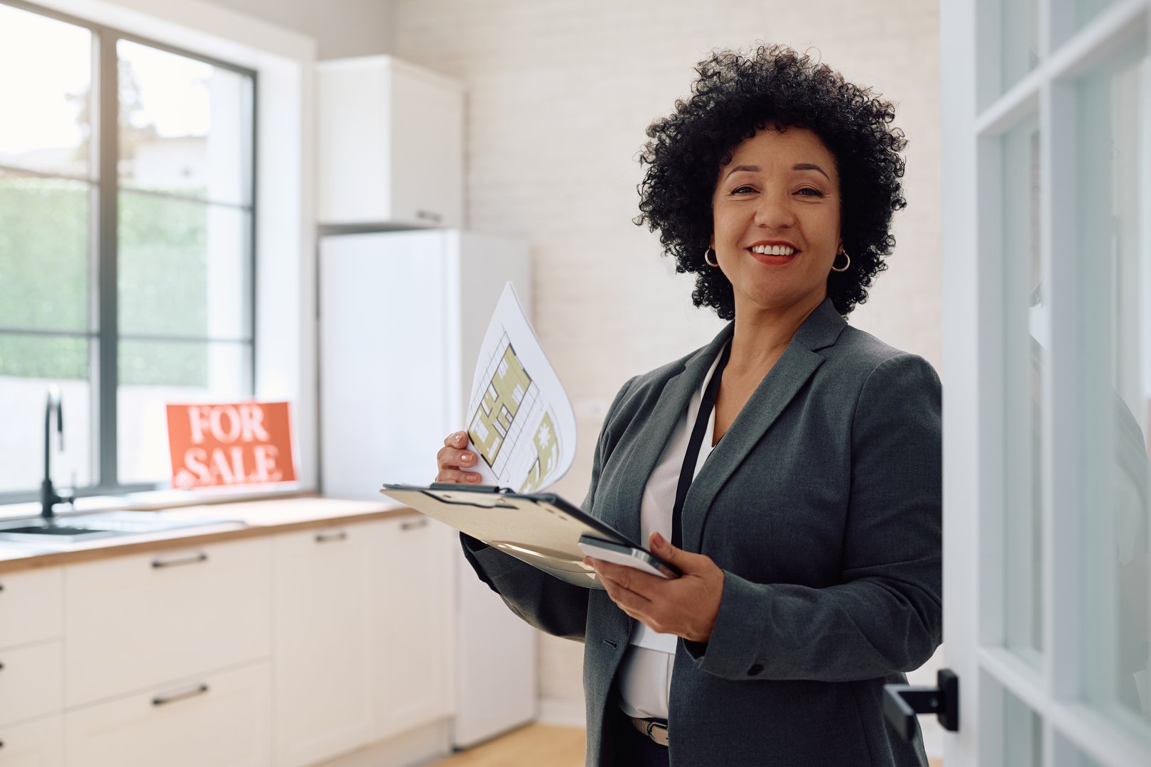 Happy real estate agent analyzing blueprints while preparing for open house day and looking at camera. Copy space.