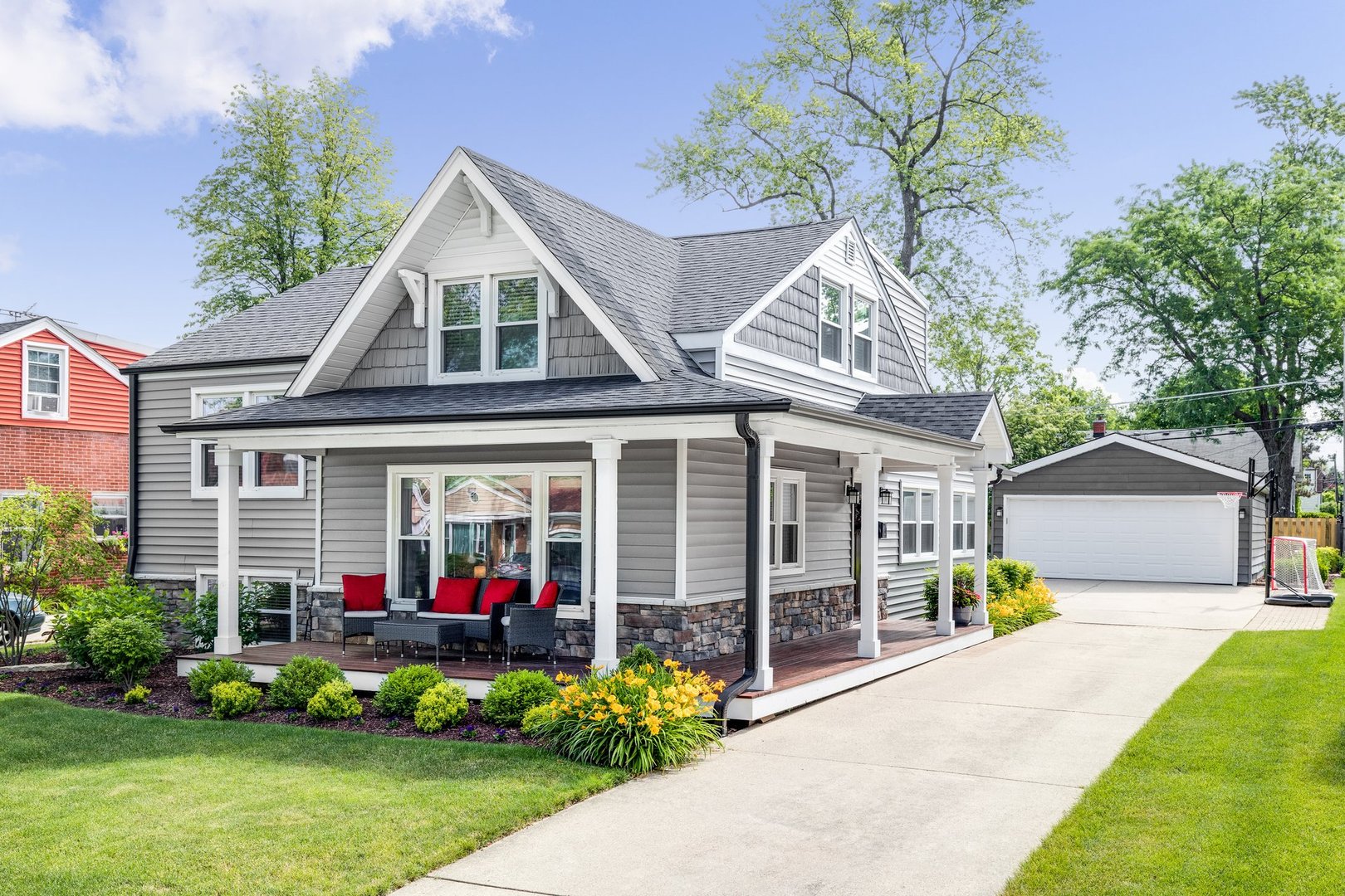 Oak Park, IL, USA - May 28, 2020: The exterior of a grey modern, suburban home with a covered porch and furniture featuring red accent pillows.