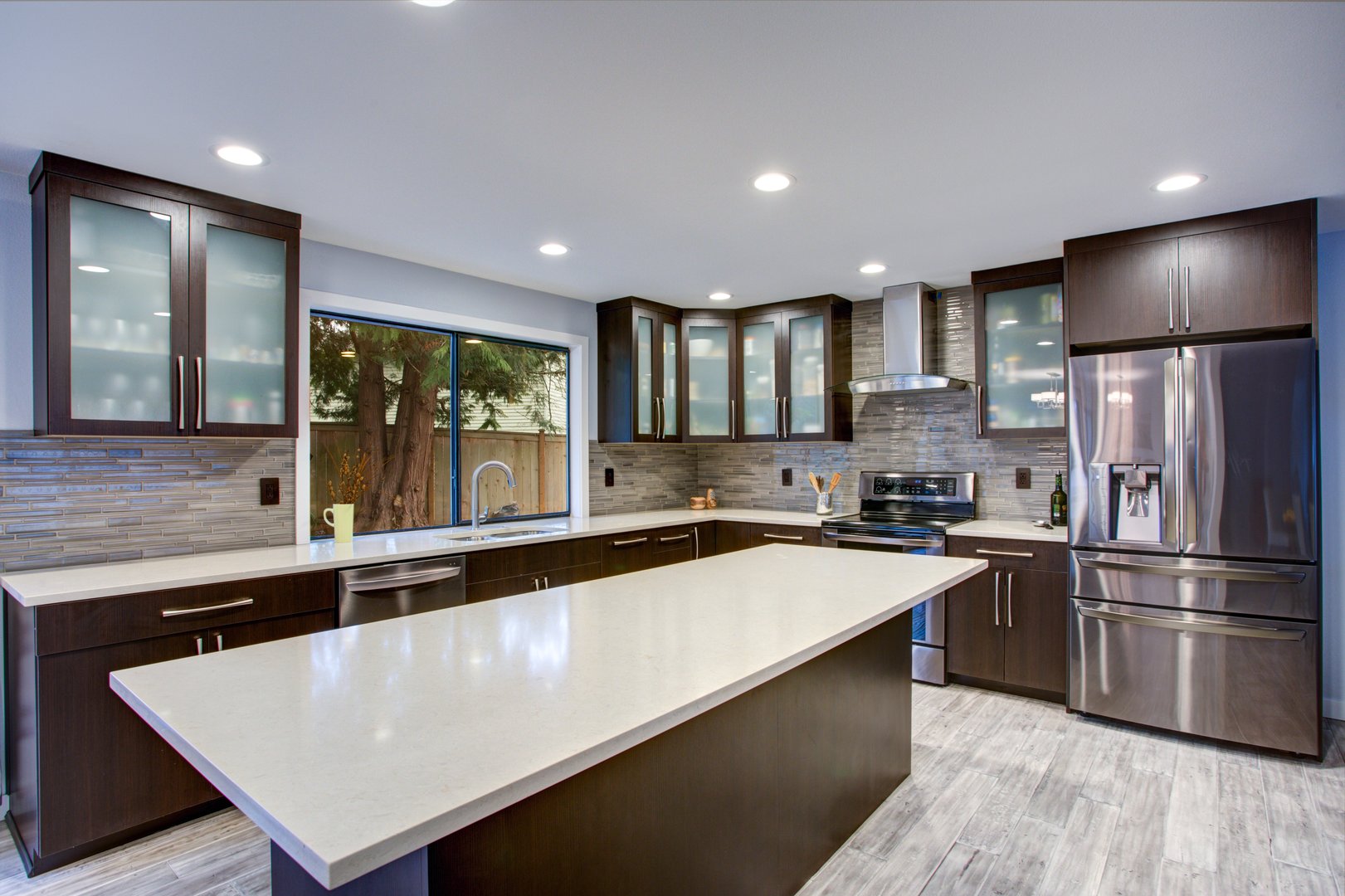 Updated contemporary kitchen room interior with white counters and dark wood cabinets fitted with luxury stainless steel appliances.