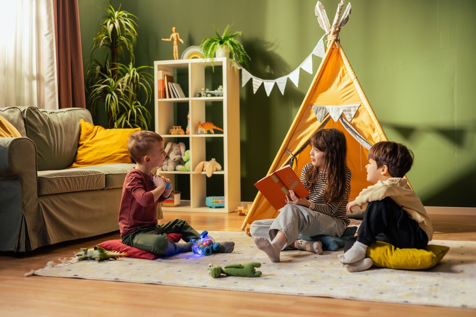 Group of happy children playing and reading book in cozy playroom with teepee tent