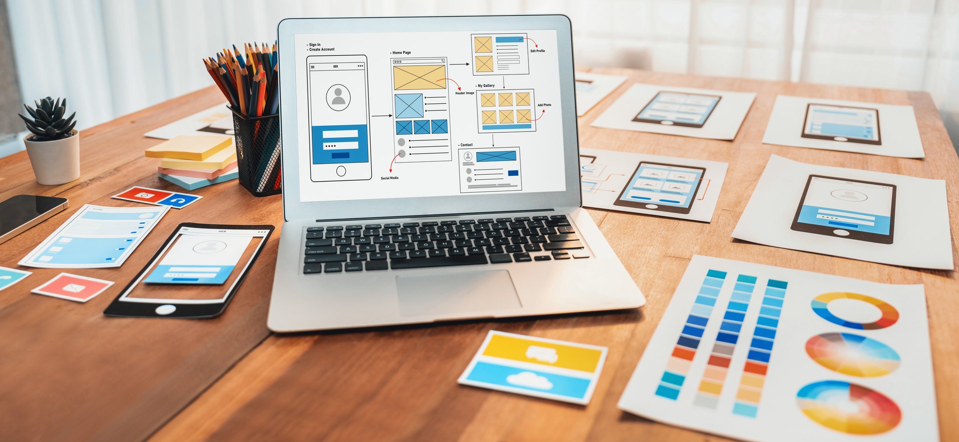 Digital and paper wireframe designs for web or mobile app UI UX display on laptop computer screen. Panoramic shot of developer workspace for brainstorming and design application framework. Scrutinize