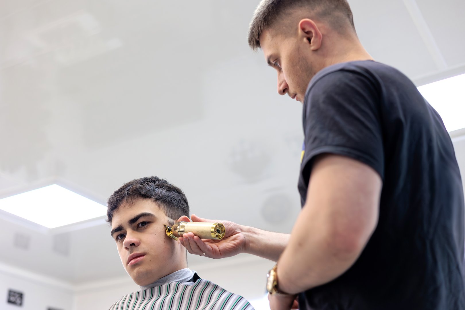 Professional Barber Giving a Haircut to a Young Client with an Electric Trimmer. Young Male Barber Cutting Teen Boy's Hair in Modern Barbershop Interior. Copyspace
