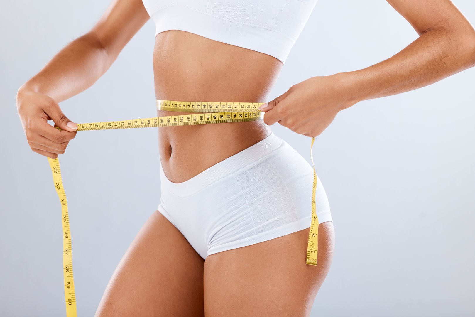 Weightloss, health and woman with measuring tape in a studio for her diet, exercise or wellness. Fitness, body and healthy slim female model checking the measurement of her waist by a gray background