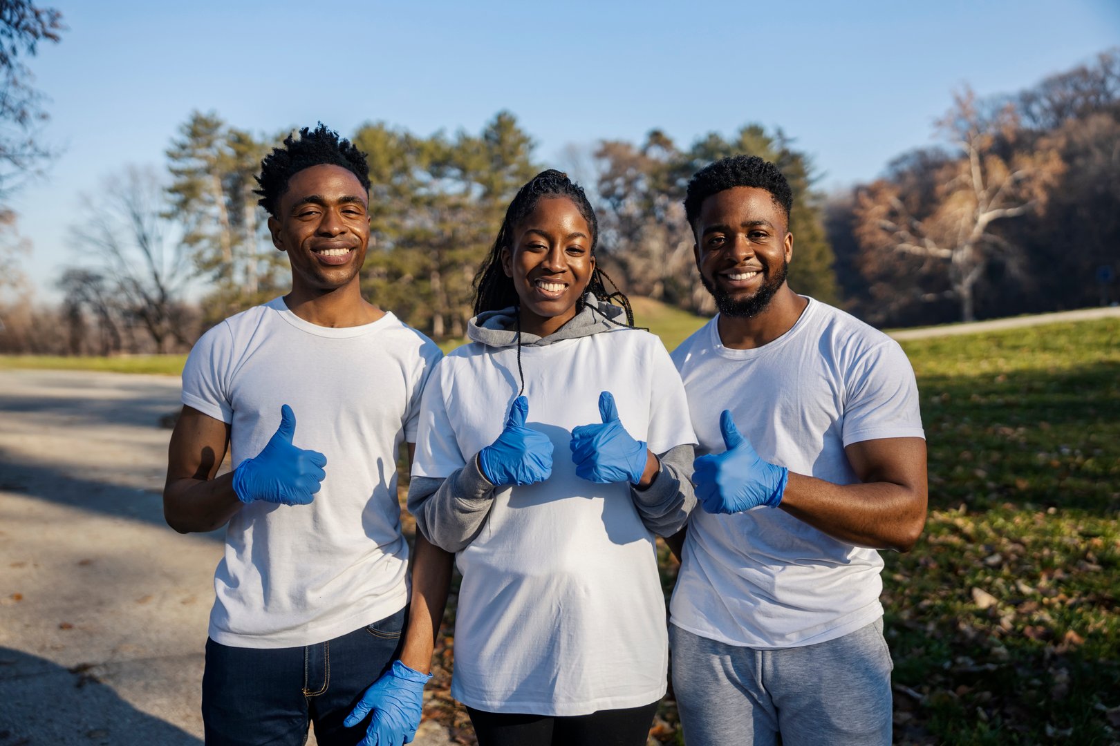 Portrait of smiling diverse eco team and activists in white shirts giving thumbs up at camera on earth's day.