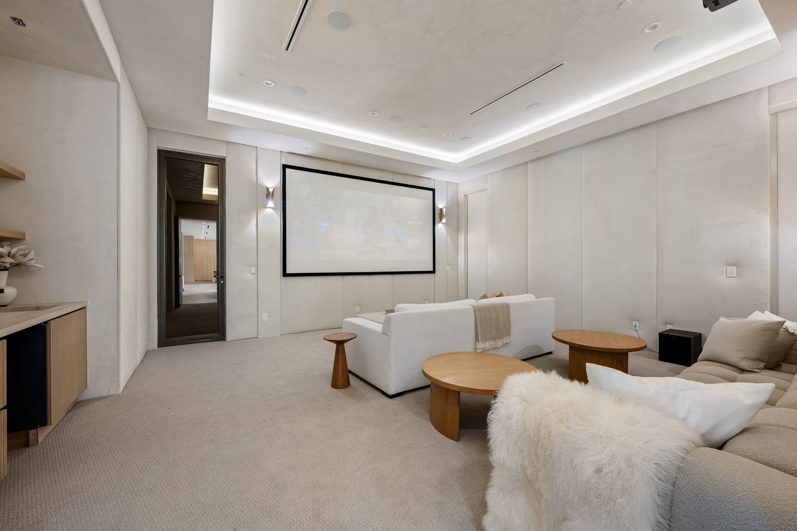Modern home theater room with comfortable seating, neutral tones, and a large screen in a luxurious setting.