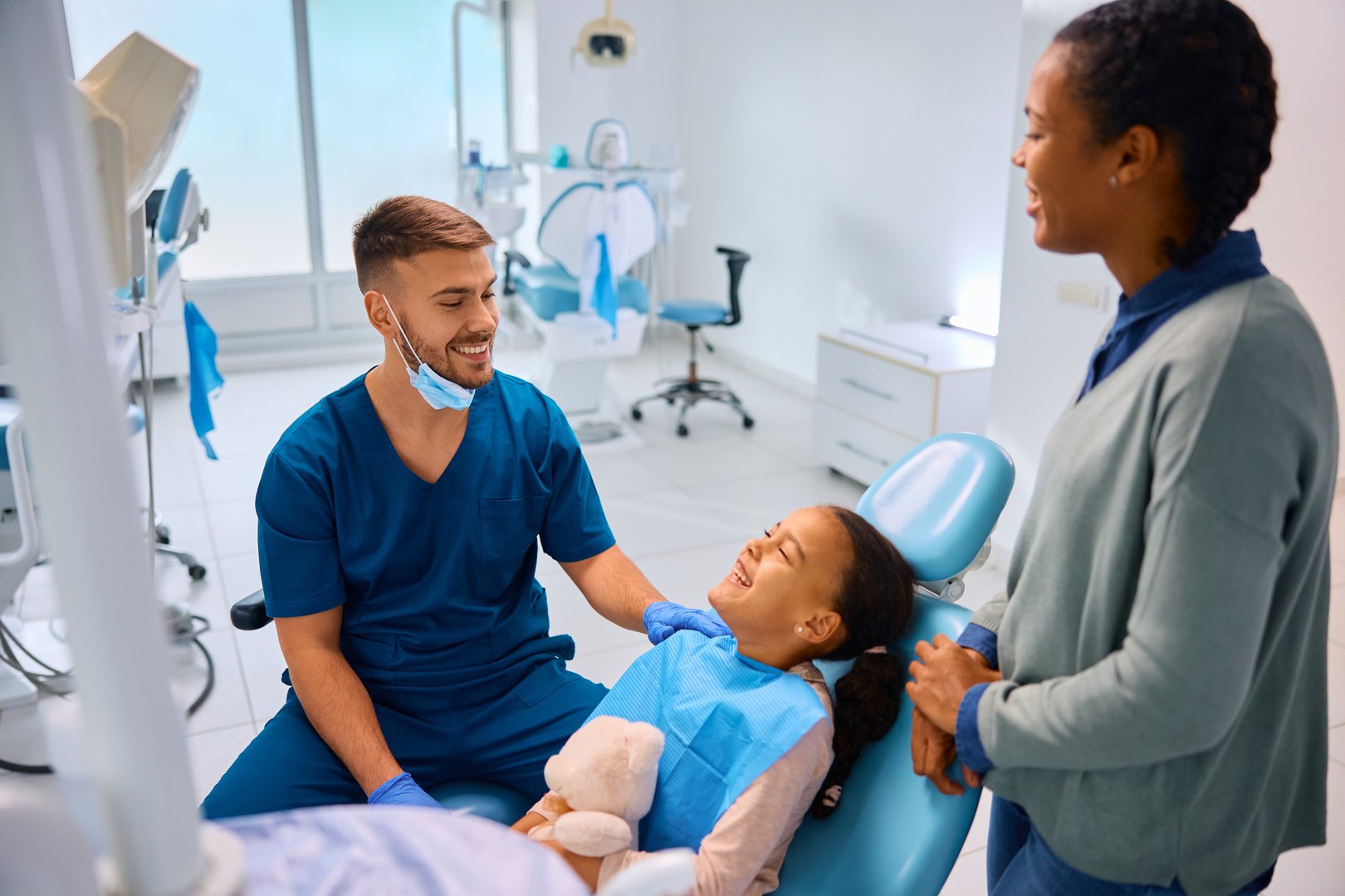 Happy dentist talking to African little girl and her mother at dental clinic