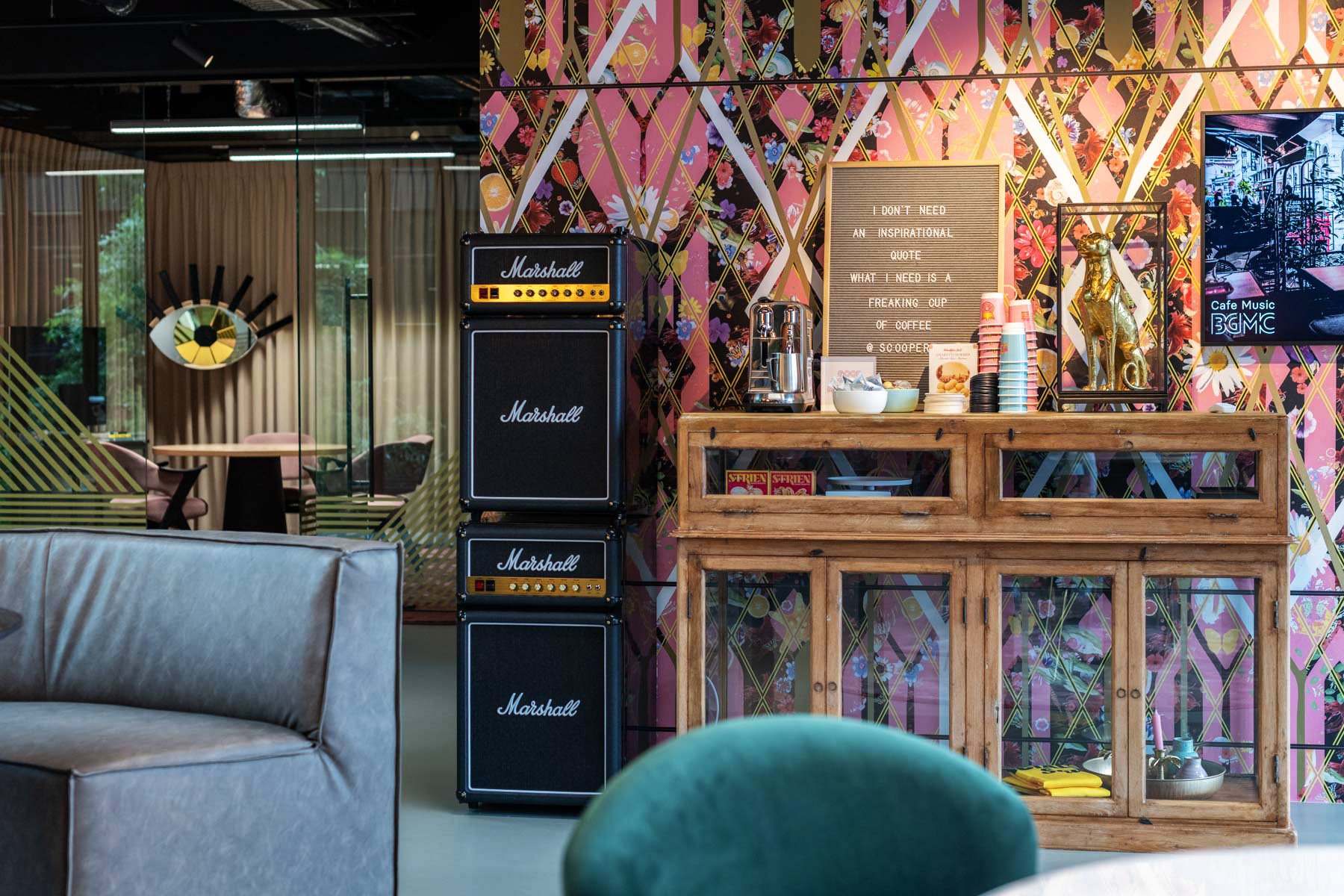 Colorful room with Marshall amplifiers, vintage wood cabinet, coffee setup, and vibrant patterned wall art.