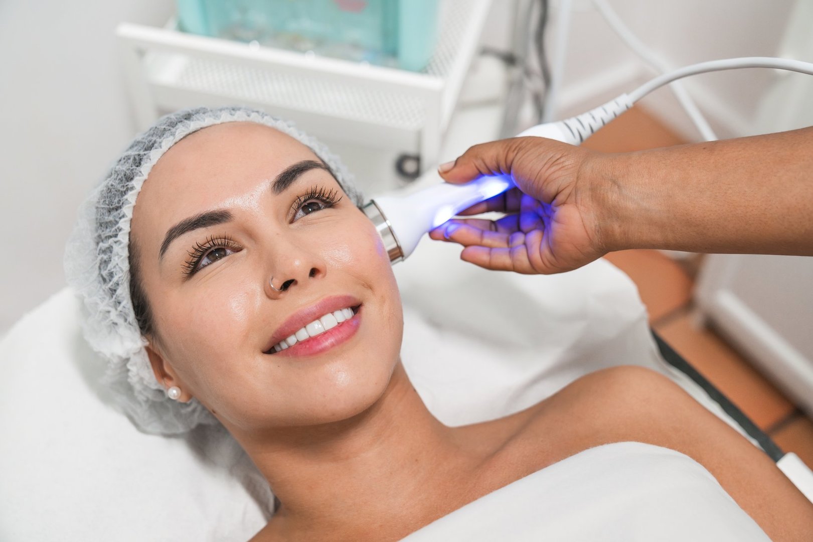 Beautician is applying a laser treatment on a smiling woman's face inside a beauty salon