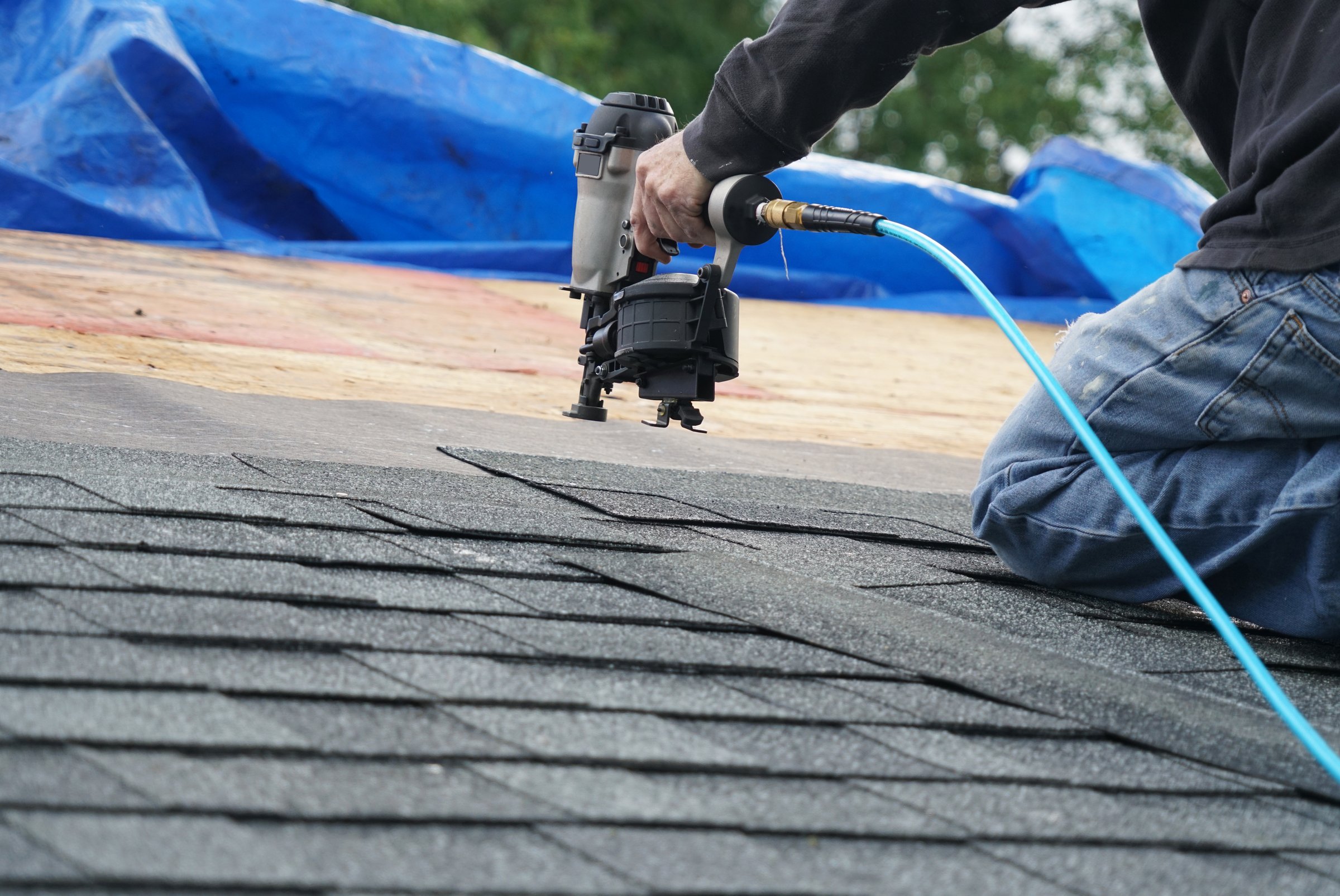Handyman using nail gun to install shingle on roof