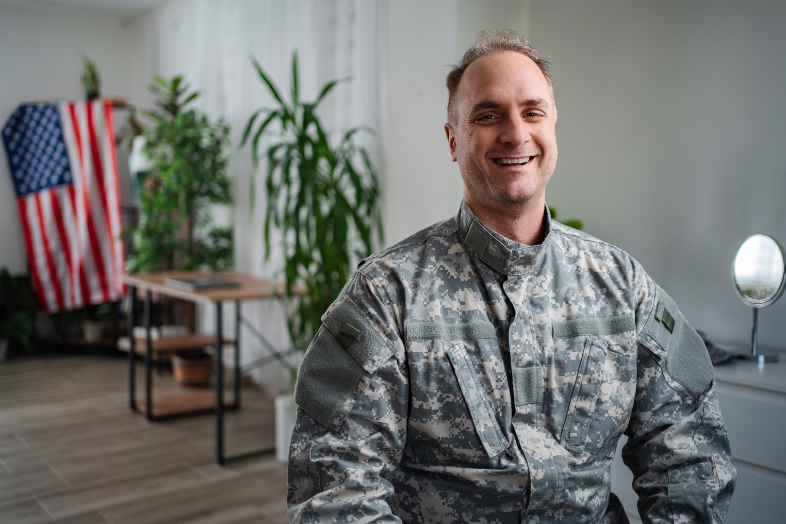 Portrait of a smiling American soldier in his home, with the American flag in the background