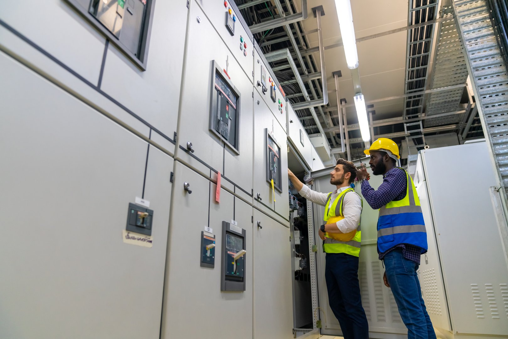 Professional electrical engineer in safety uniform working at factory server electric control panel room. Industrial technician worker maintenance checking power system at manufacturing plant room.