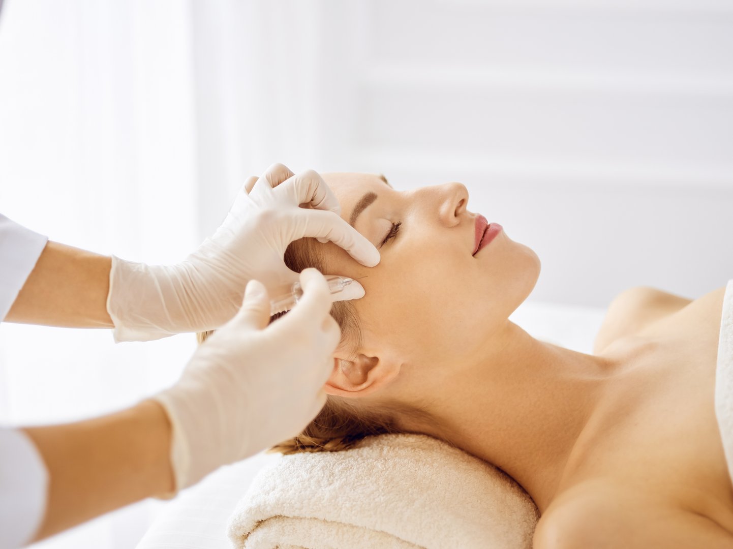Beautiful woman receiving beauty injections with closed eyes. Beautician doctor hands doing beauty procedure to female face with syringe. Cosmetic medicine and surgery concept.