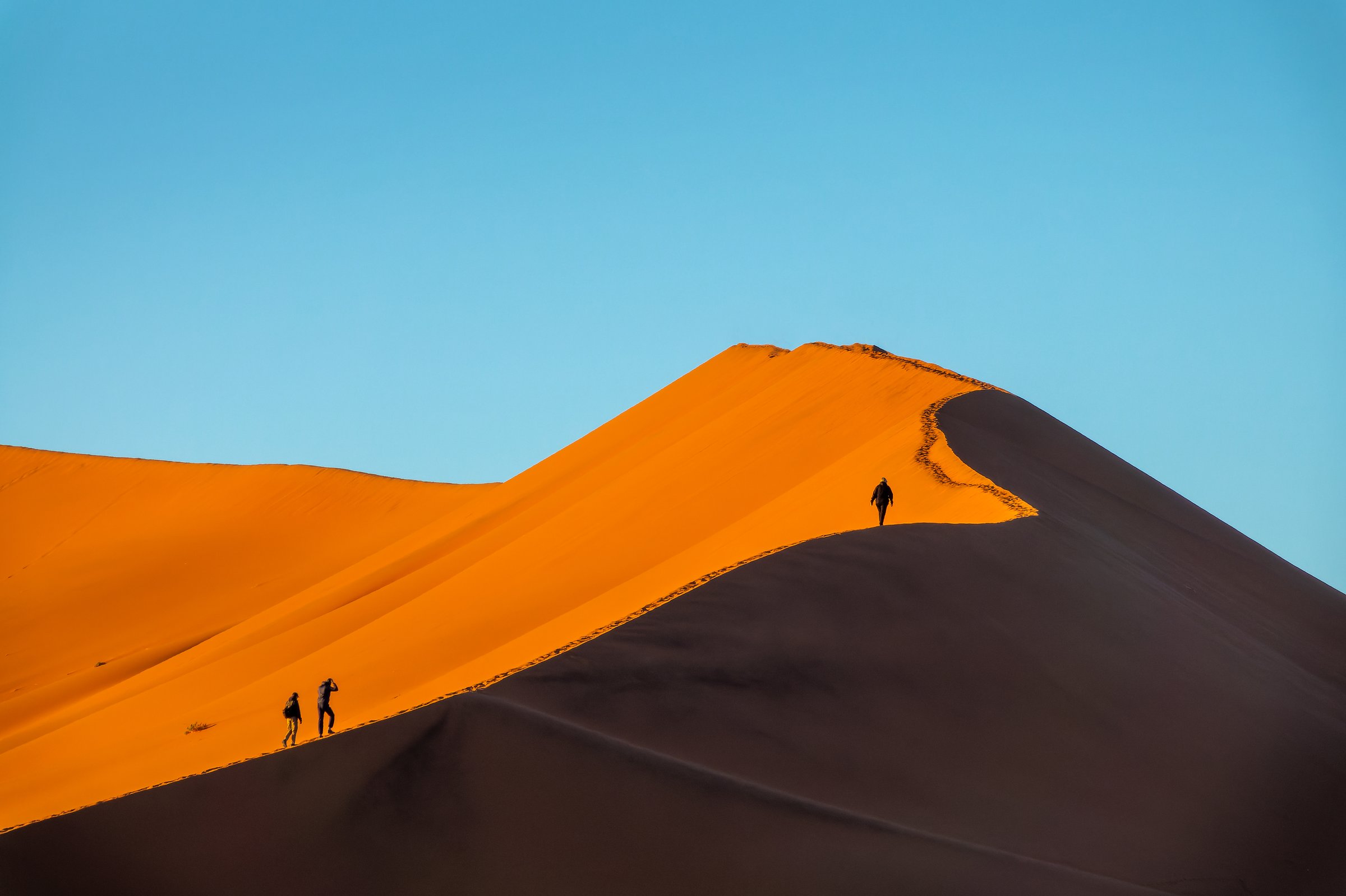 Silhouettes of people climbing Big Daddy sand dune at sunrise in Sossusvlei, Namib Naukluft national park, Namibia scenic landscape, Africa