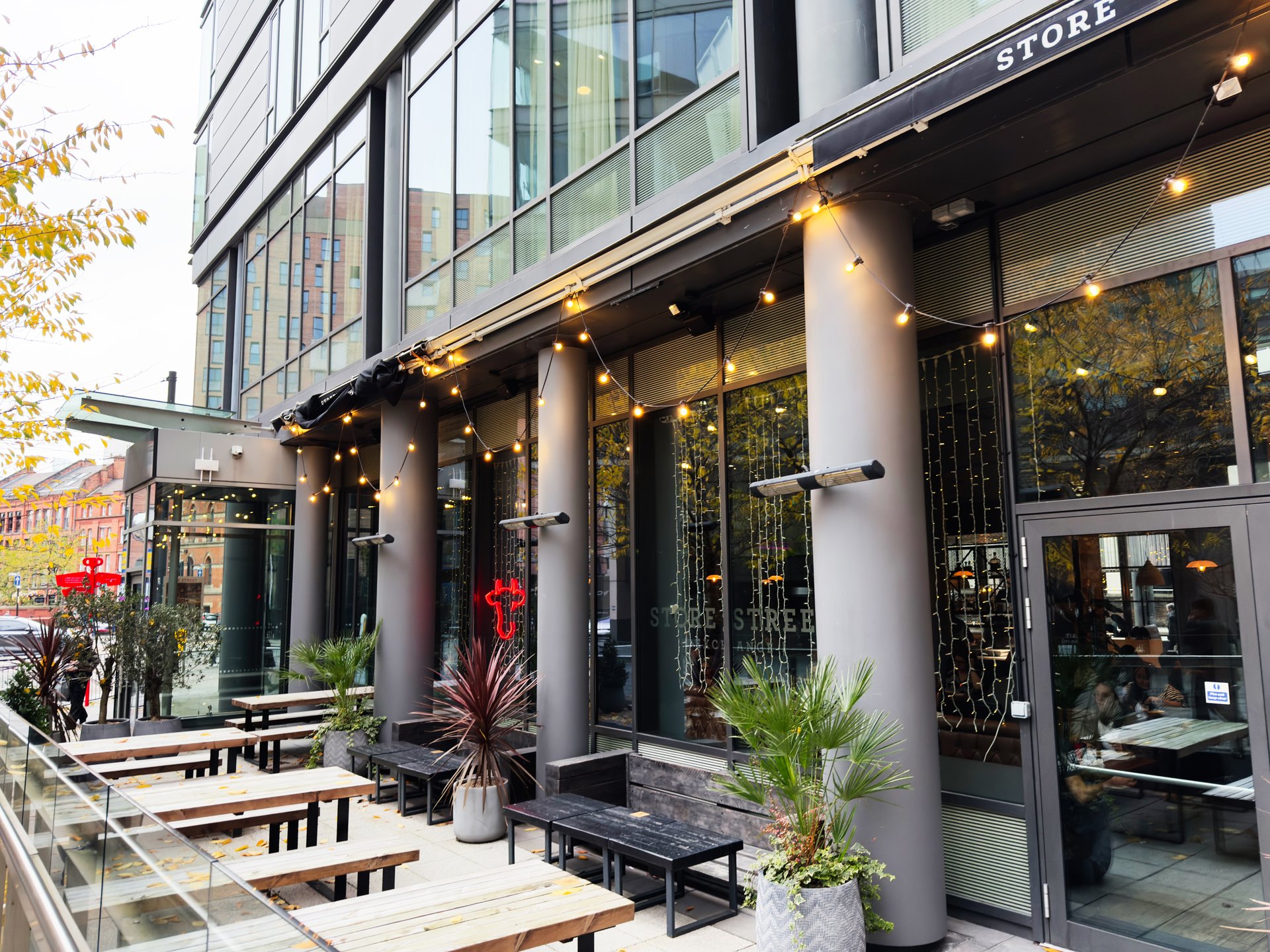 Manchester, UK - November 07, 2025: Bustling urban cafe scene in Manchester with lights, plants, and casual dining outdoors.