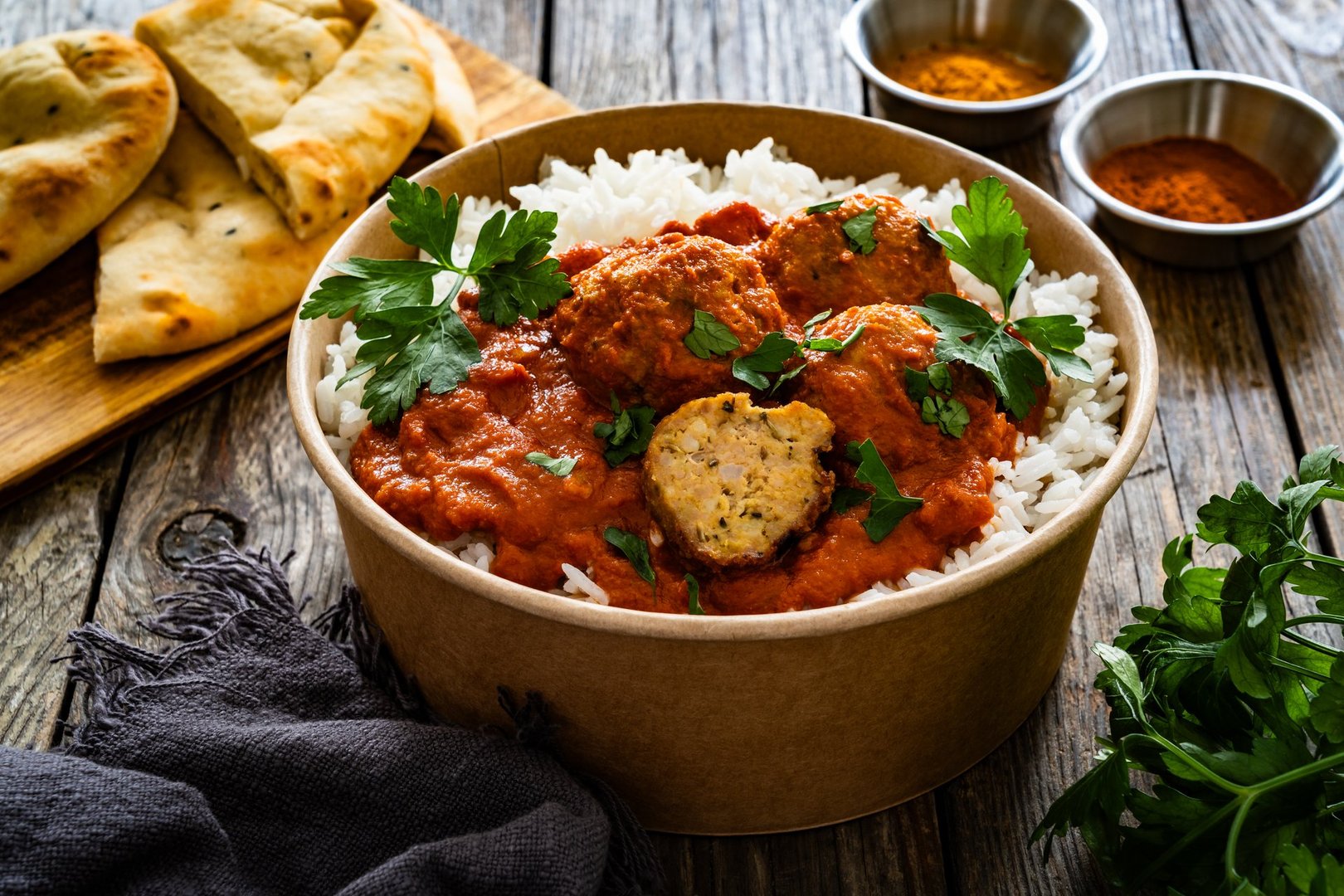 Butter chicken curry meatballs with rice in box to go on wooden table. Takeaway indian food