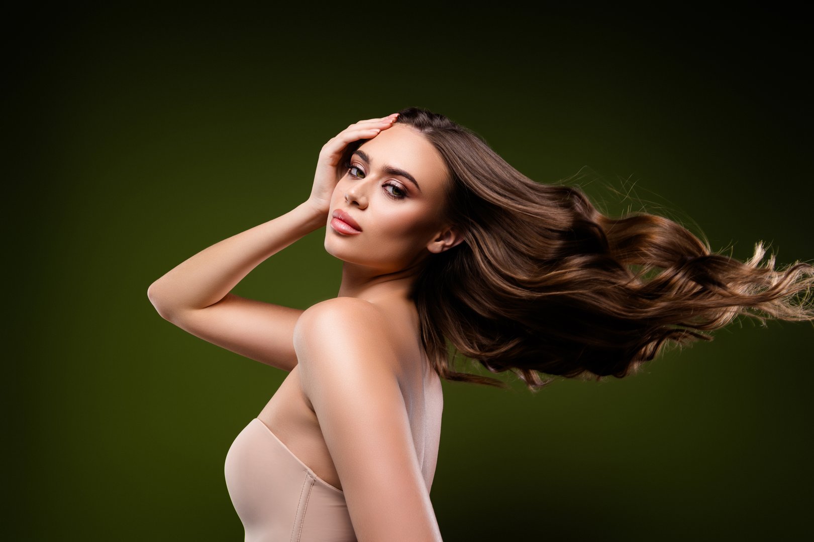 A stylish and glamorous young brunette woman with flowing hair poses gracefully. Presented against a green background with subtle highlights, highlighting her stunning beauty and confident charm.